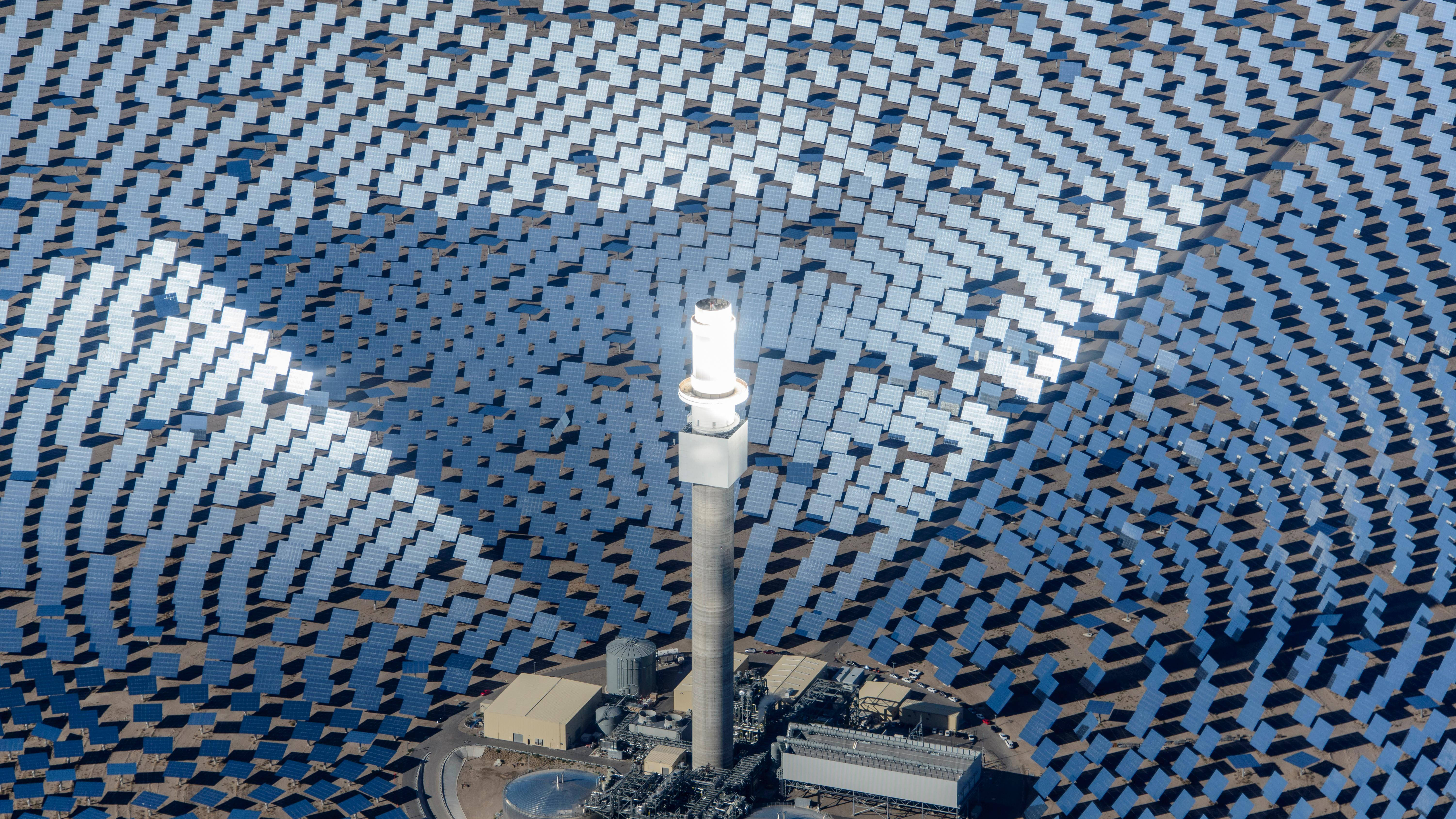 電力 桌布 壁紙 — 從空中俯瞰一座太陽能發電廠，數千塊藍色反光板圍繞中央塔樓排列成同心圓。