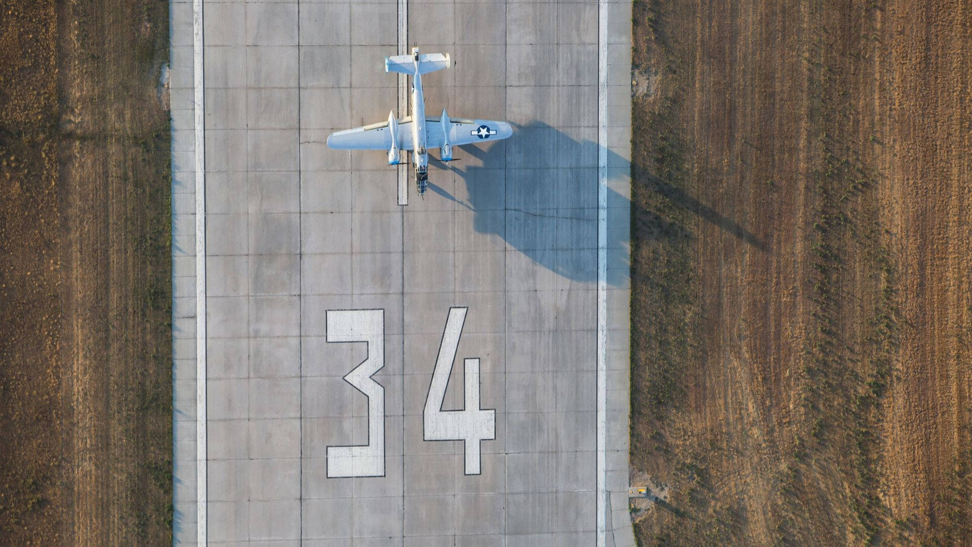 Runway 桌布 壁紙 — 從空中俯瞰一架復古軍用飛機停在34號跑道上，在混凝土上投下長長的影子。