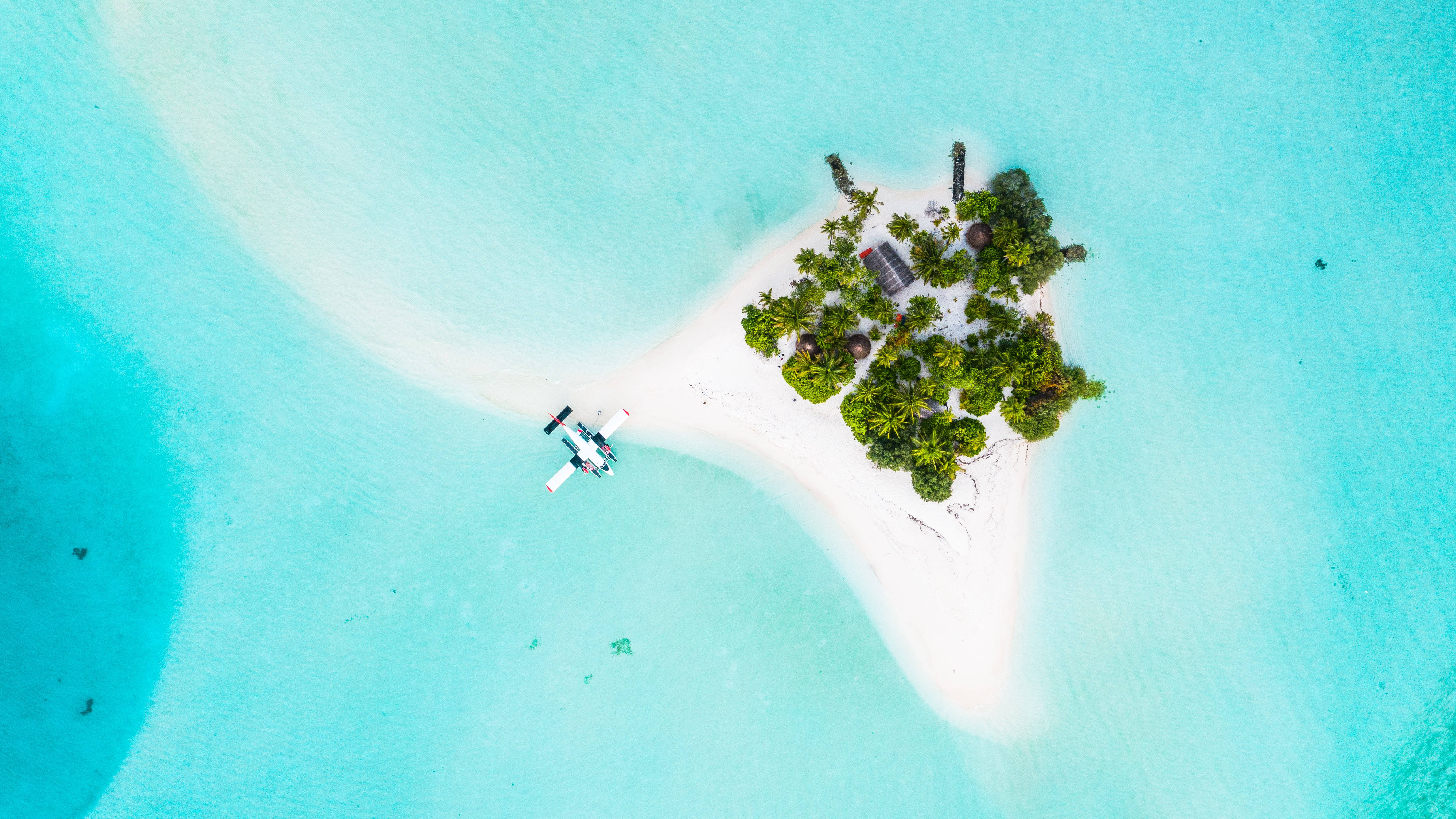 馬爾地夫 桌布 壁紙 — 從空中俯瞰一架水上飛機降落在碧綠海水旁、鬱蔥熱帶島嶼邊的純白沙洲上。