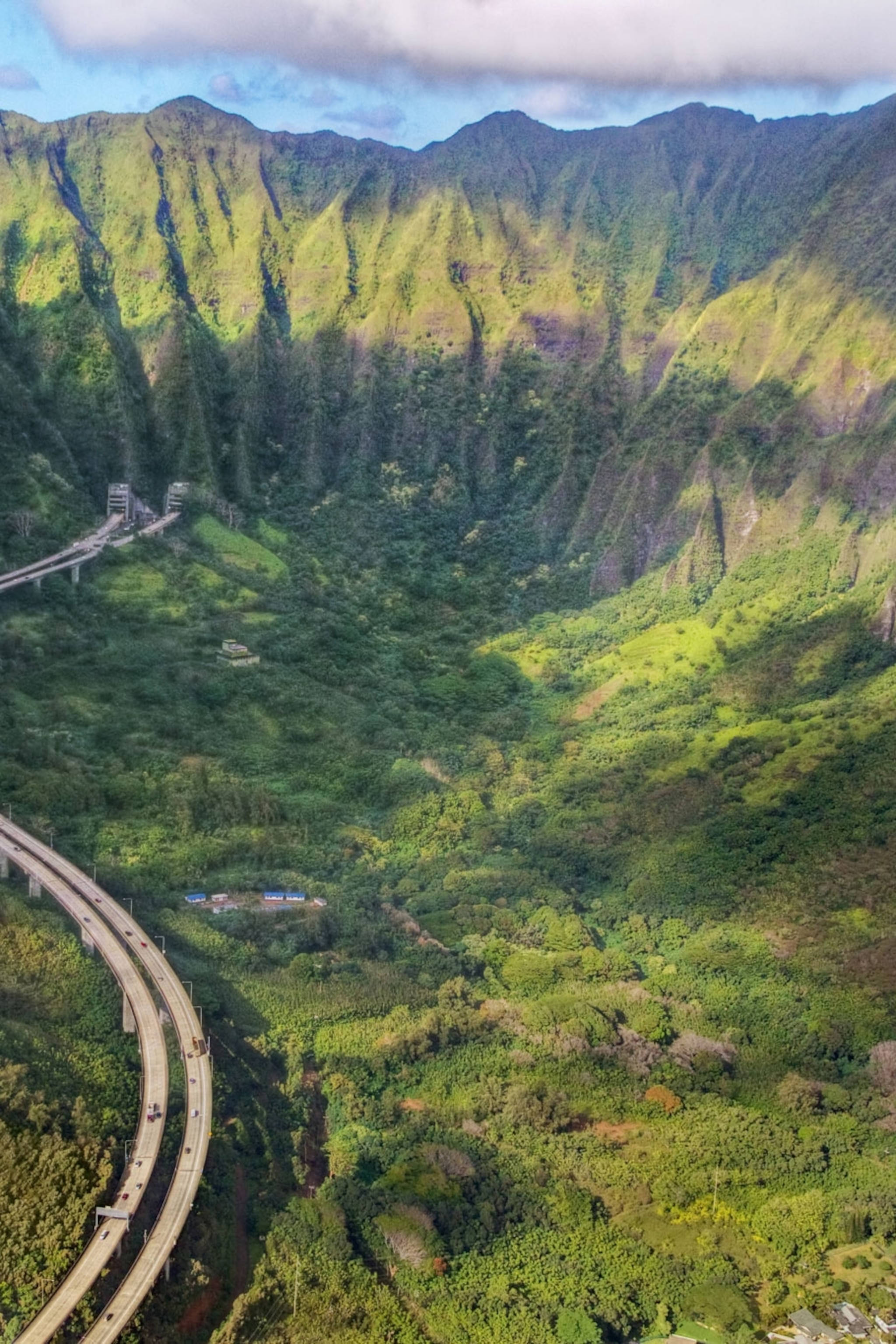 山脈 桌布 壁紙 — 從空中俯瞰一條蜿蜒的高速公路穿過鬱鬱蔥蔥的綠色山谷，天空部分多雲。