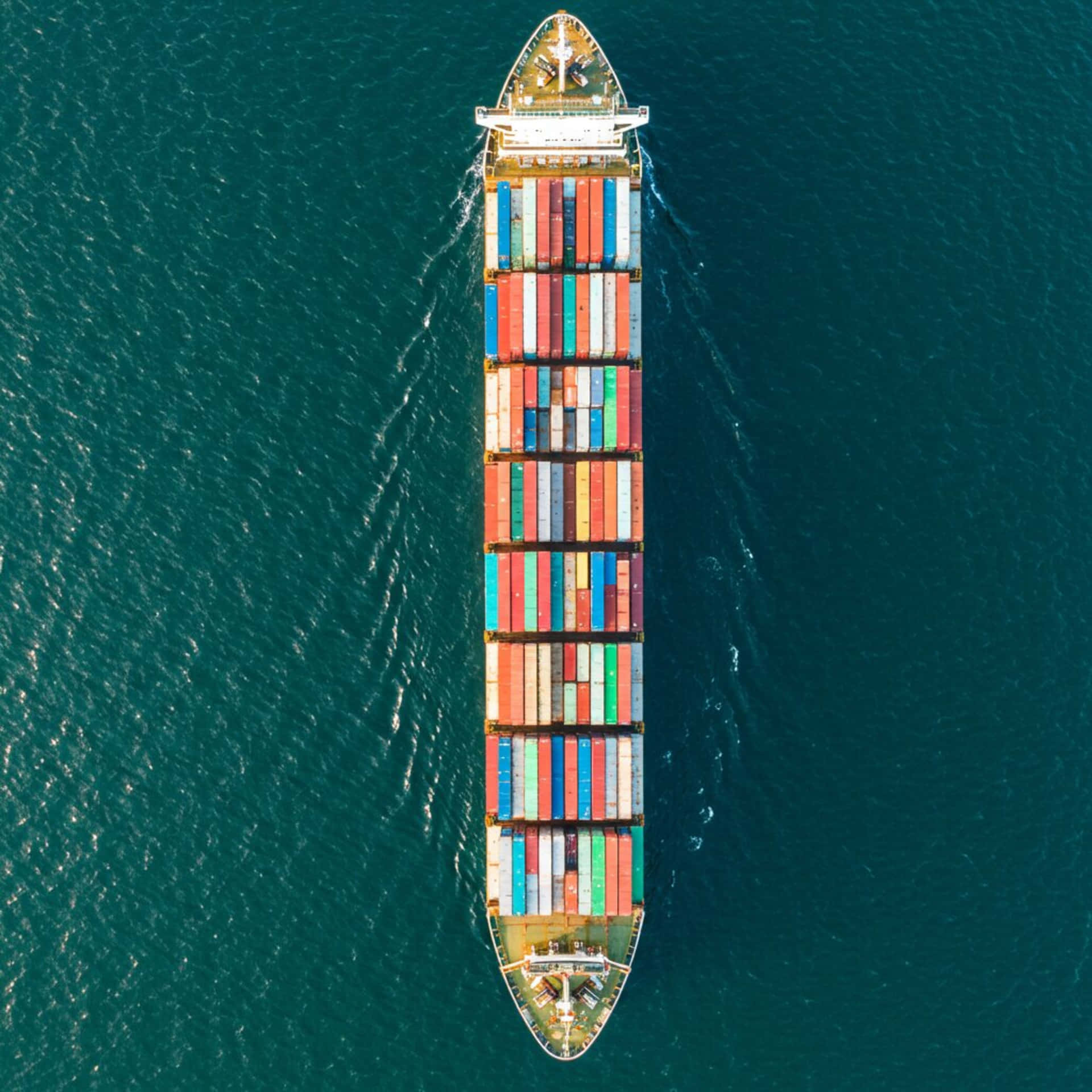 Container ship 壁紙 — 從空中俯瞰一艘大型貨櫃船在深藍綠色海洋中航行，留下白色尾跡。