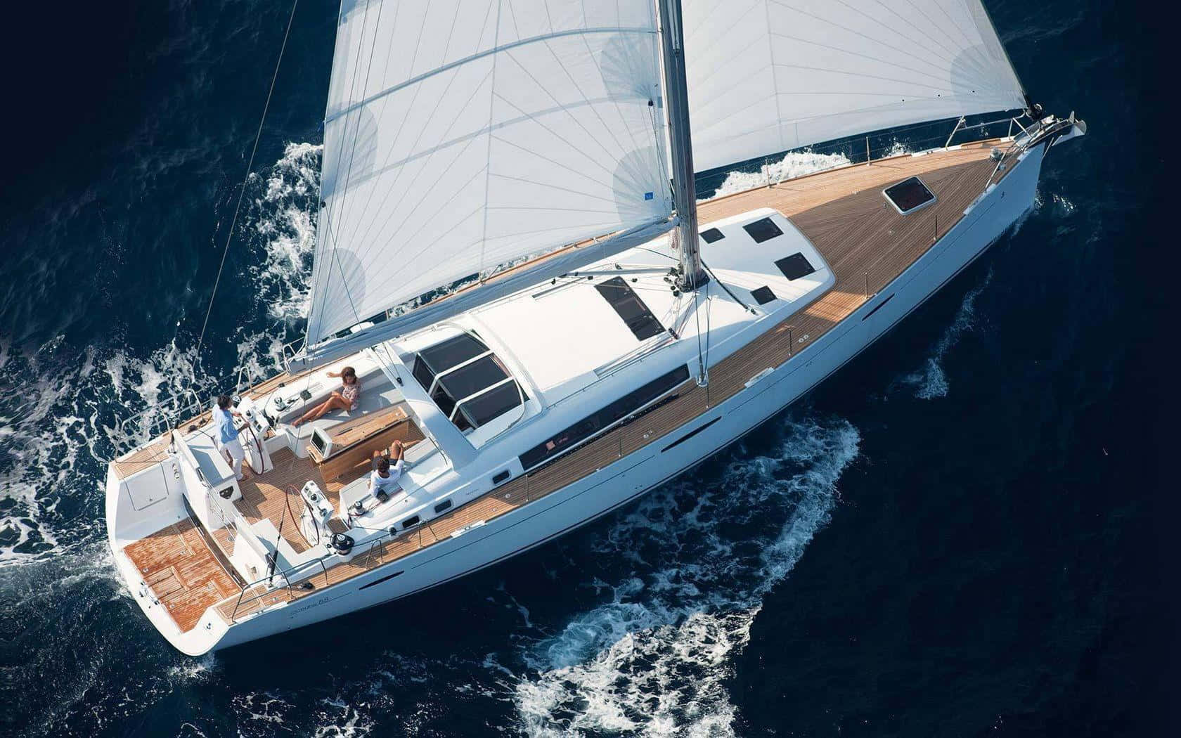 Yacht 桌布 壁紙 — 從空中俯瞰一艘豪華帆船，白色帆布劃破深藍色海浪，人們在甲板上放鬆。