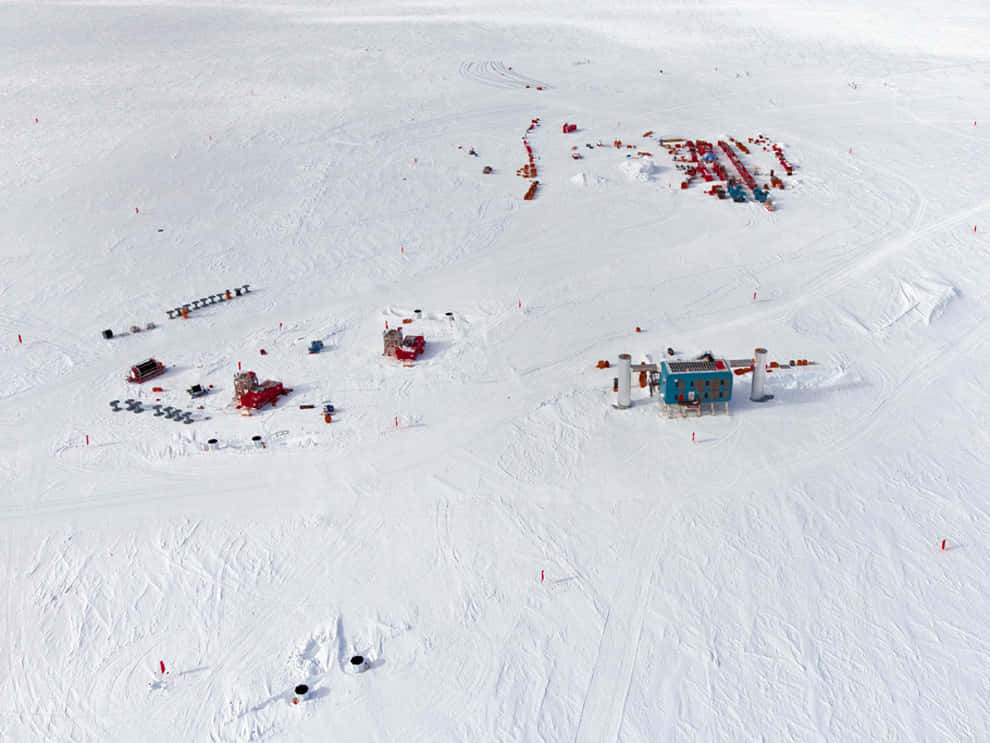 South Pole 桌布 壁紙 — 從空中俯瞰偏遠的雪地研究站，紅色設備和藍色建築散落在無盡的白色冰面上。