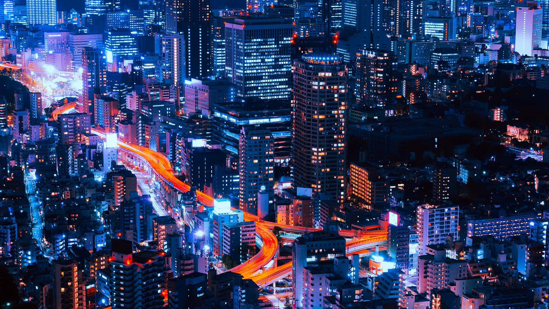 City Night 桌布 壁紙 — 從空中俯瞰夜晚霓虹燈照亮的天際線，閃爍的摩天大樓和交通留下的鮮豔橙色光軌。