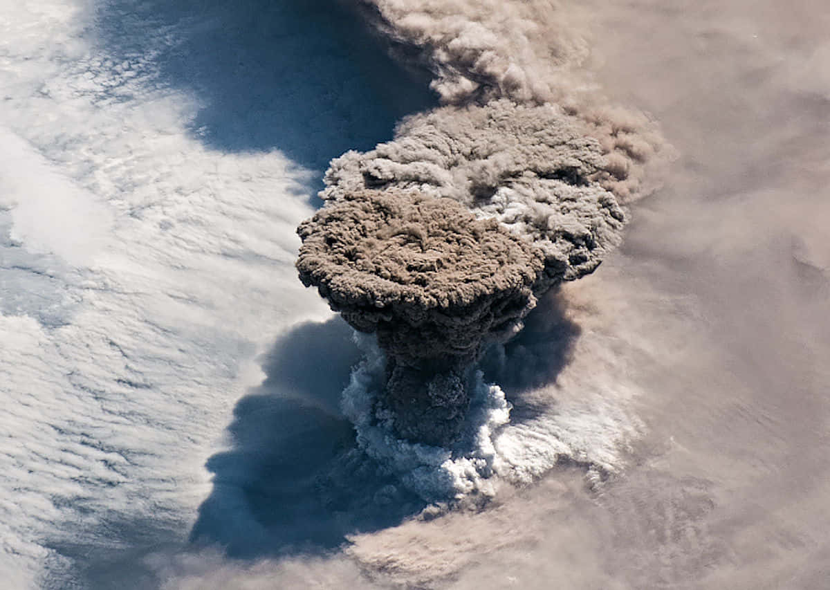 Volcano 桌布 壁紙 — 從空中俯瞰大規模火山爆發，將濃密的火山灰雲送入旋轉雲層上方的天空。