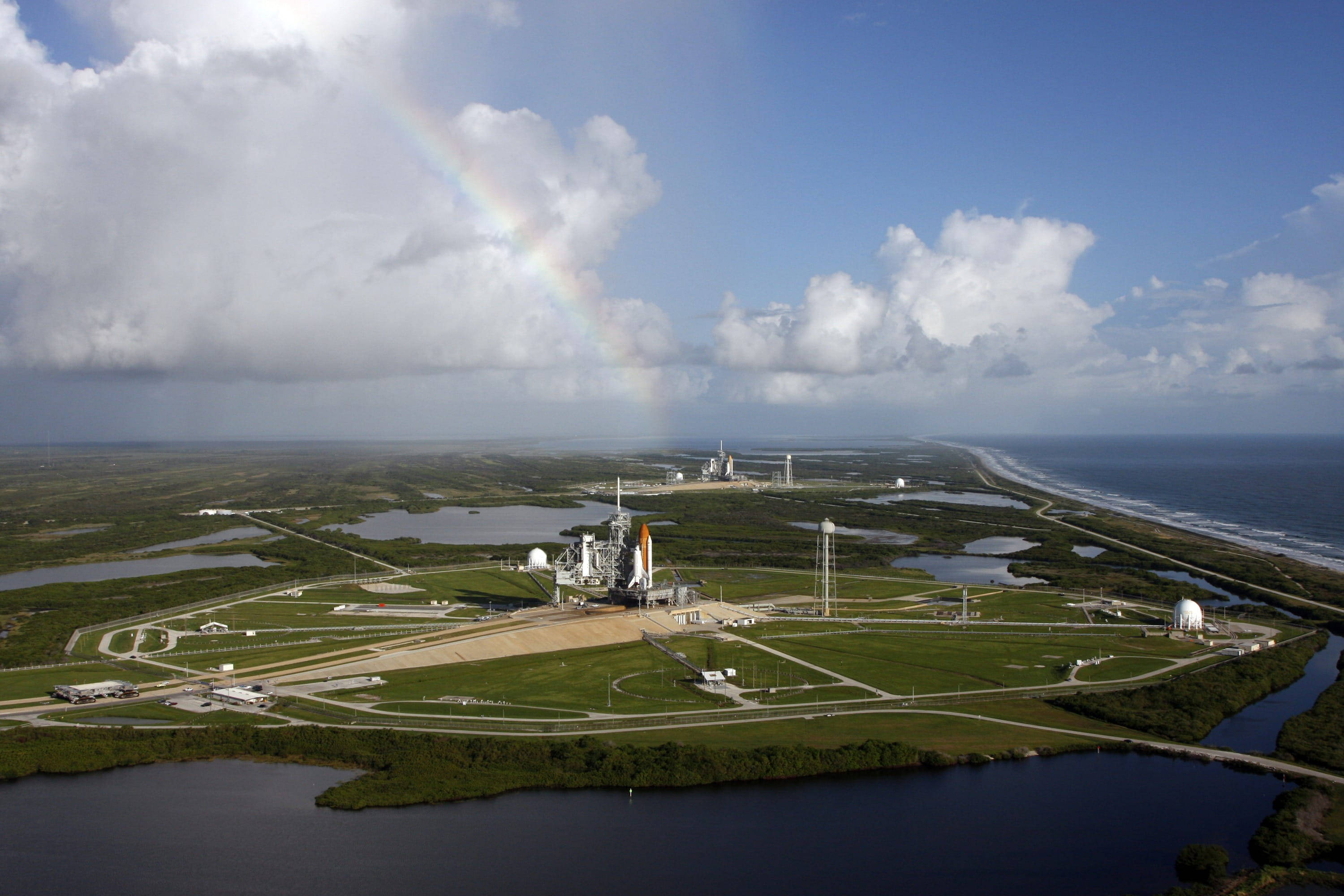 Nasa 桌布 壁紙 — 從空中俯瞰太空發射場，一道鮮豔的彩虹橫跨沿海沼澤地和海洋。