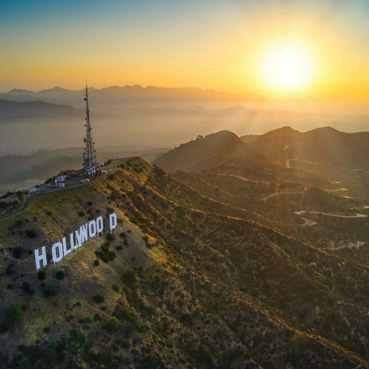 好萊塢 桌布 壁紙 — 從空中俯瞰好萊塢標誌在金色夕陽光芒中閃耀，位於霧氣繚繞的山脊之上。