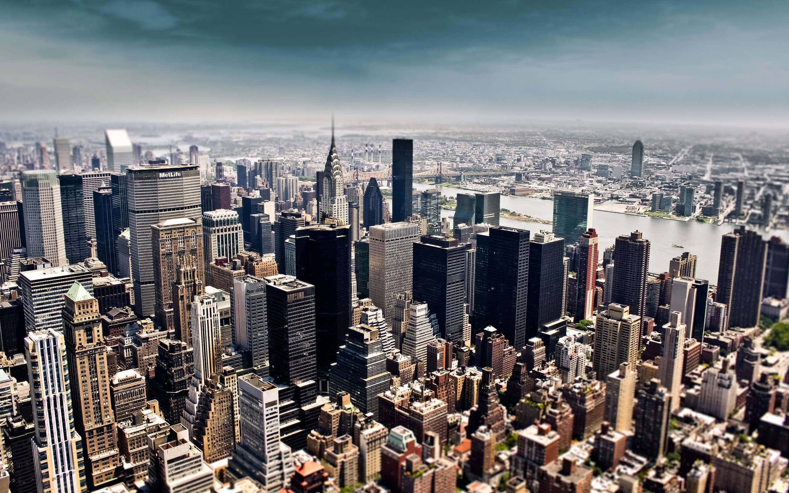 New York 桌布 壁紙 — 從空中俯瞰密集的城市天際線，高聳的摩天大樓和蜿蜒穿過城市的河流，天空多雲。