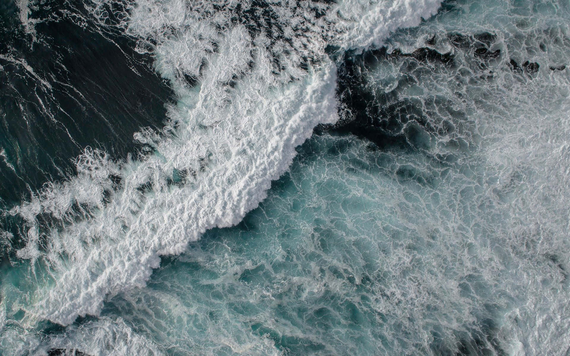 Ocean Waves 桌布 壁紙 — 從空中俯瞰洶湧的海浪，白色泡沫拍打著深藍綠色和黑色的海水。
