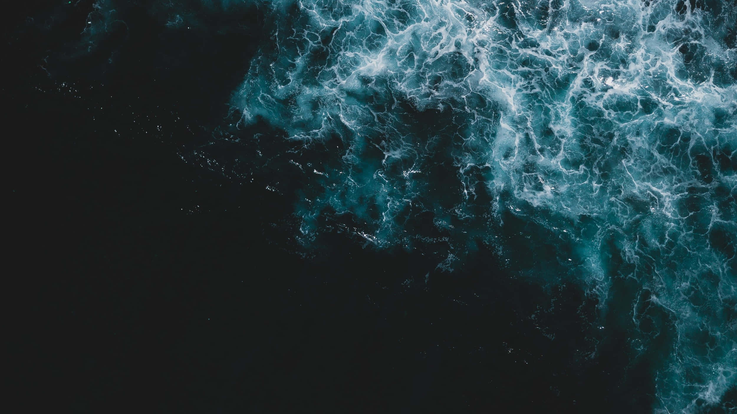Ocean Water 桌布 壁紙 — 從空中俯瞰洶湧的海浪拍打深藍綠色海水，形成泡沫般的白色浪尖。