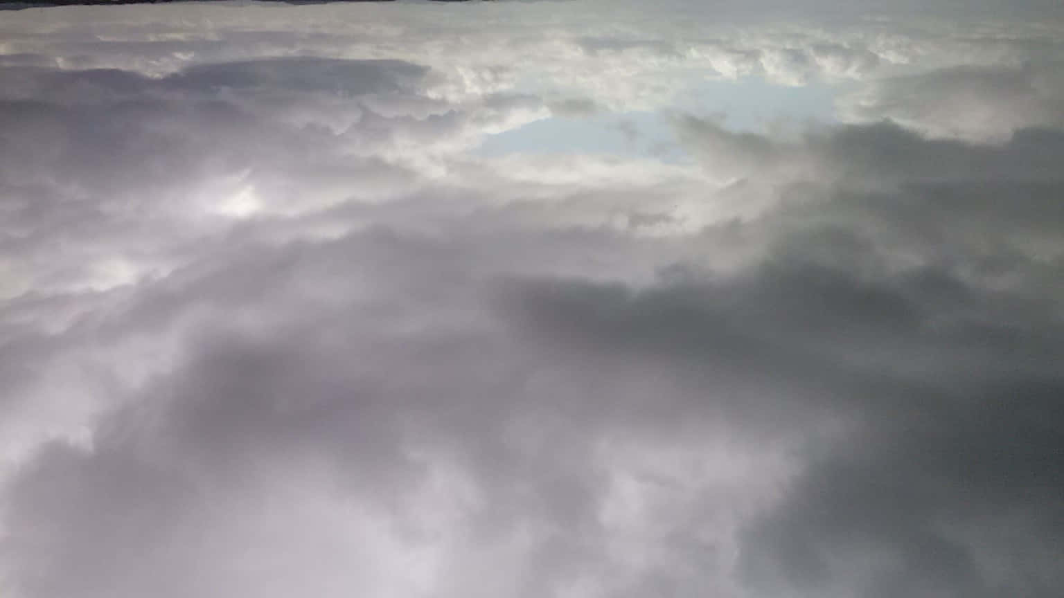 STORM-2 壁紙 — 從空中俯瞰無盡翻滾的雲層，呈現柔和的灰色和白色，淡藍色的天空斑塊隱約可見。