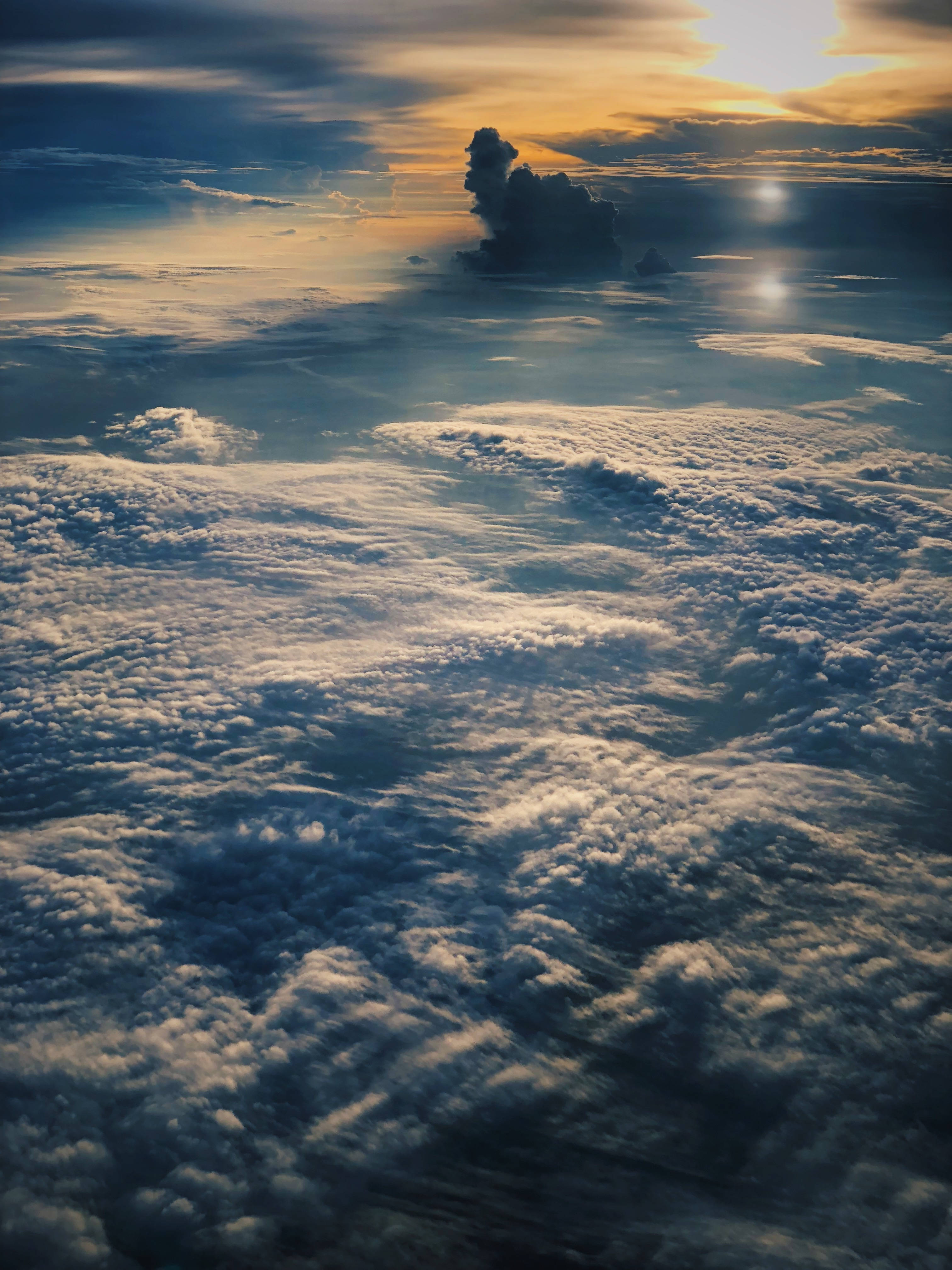 雲朵 桌布 壁紙 — 從空中俯瞰無盡雲海，沐浴在金色夕陽光芒中，孤獨的烏雲剪影映襯著發光的地平線。