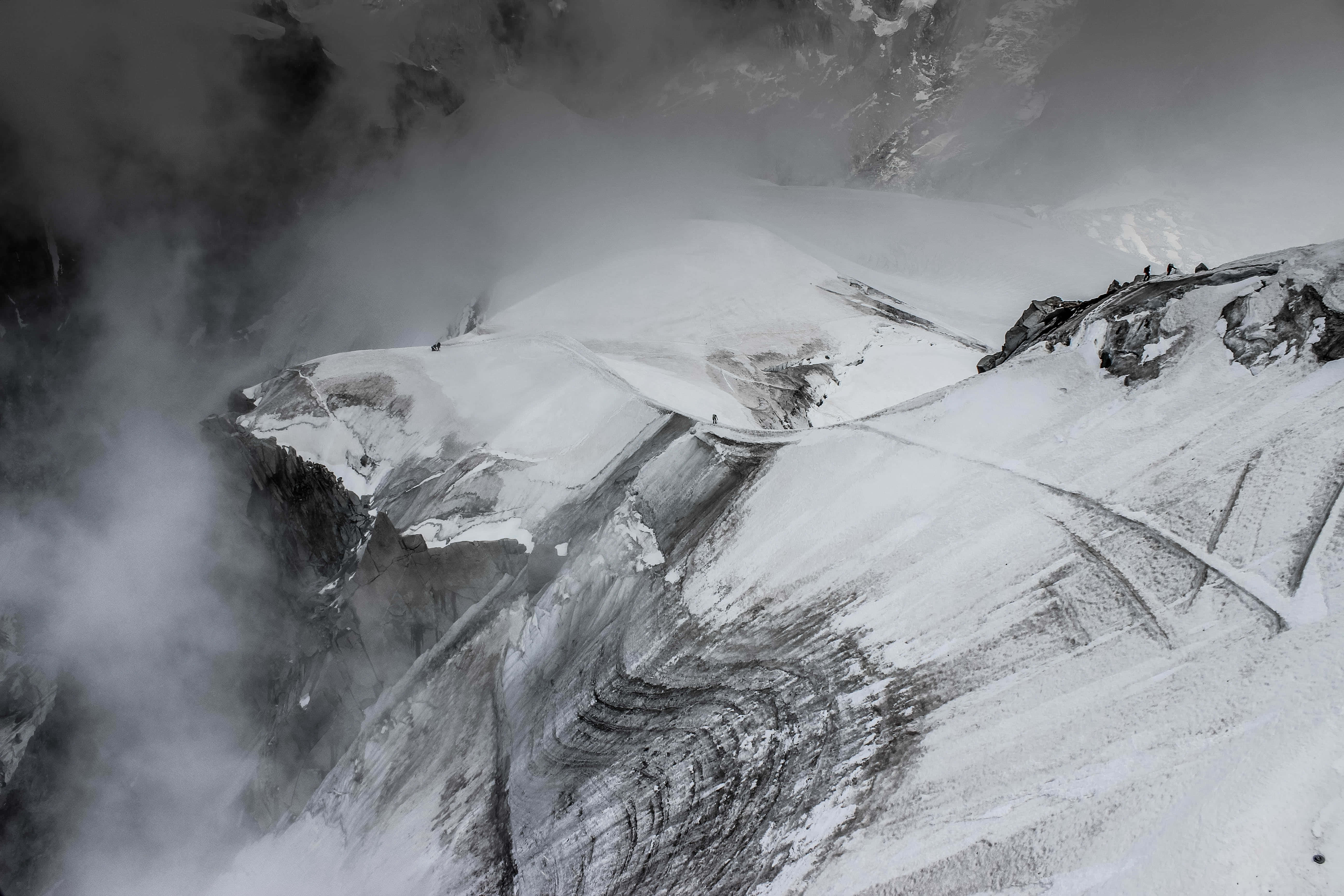 山景 桌布 壁紙 — 從空中俯瞰登山者穿過霧雲攀登冰雪覆蓋的山脊。