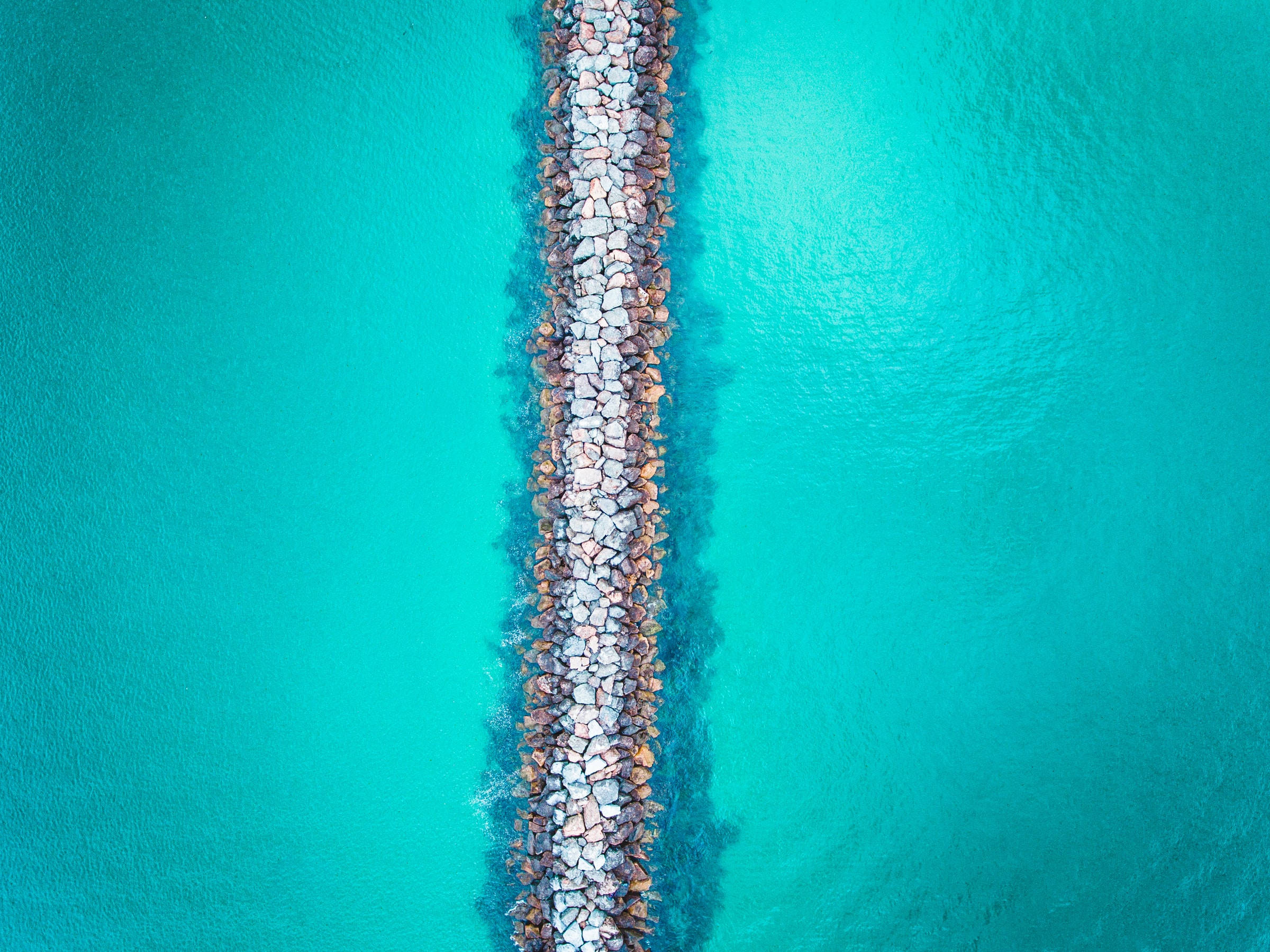 海洋藍 桌布 壁紙 — 從空中俯瞰石頭防波堤將充滿活力的藍綠色海水分成兩個對稱的部分。