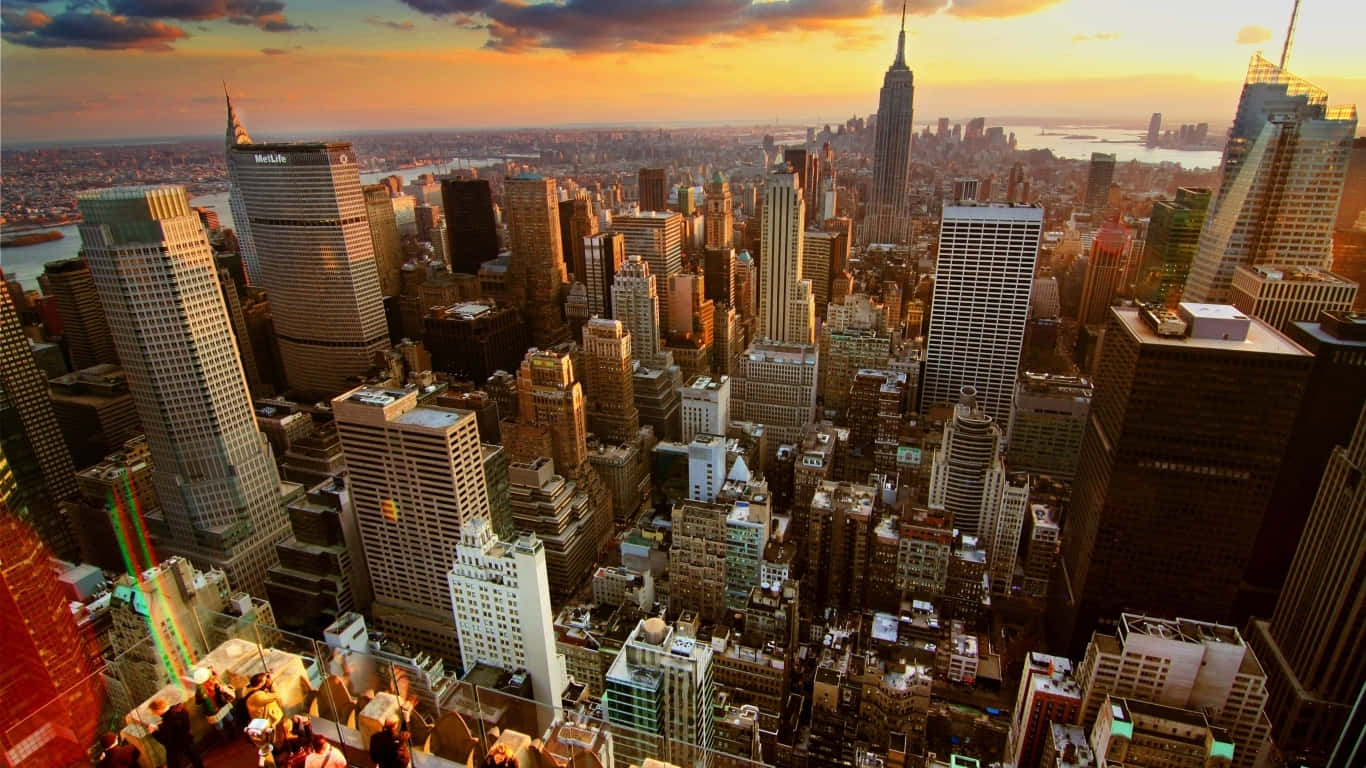 1366x768 Empire State Building 桌布 壁紙 — 從空中俯瞰紐約市天際線，夕陽西下，金色光芒灑滿摩天大樓和遠方的河流。
