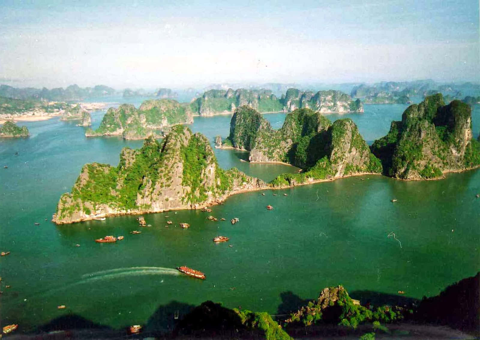 島嶼 桌布 壁紙 — 從空中俯瞰翠綠海水點綴著茂密的喀斯特島嶼，小船在寧靜海灣中航行。