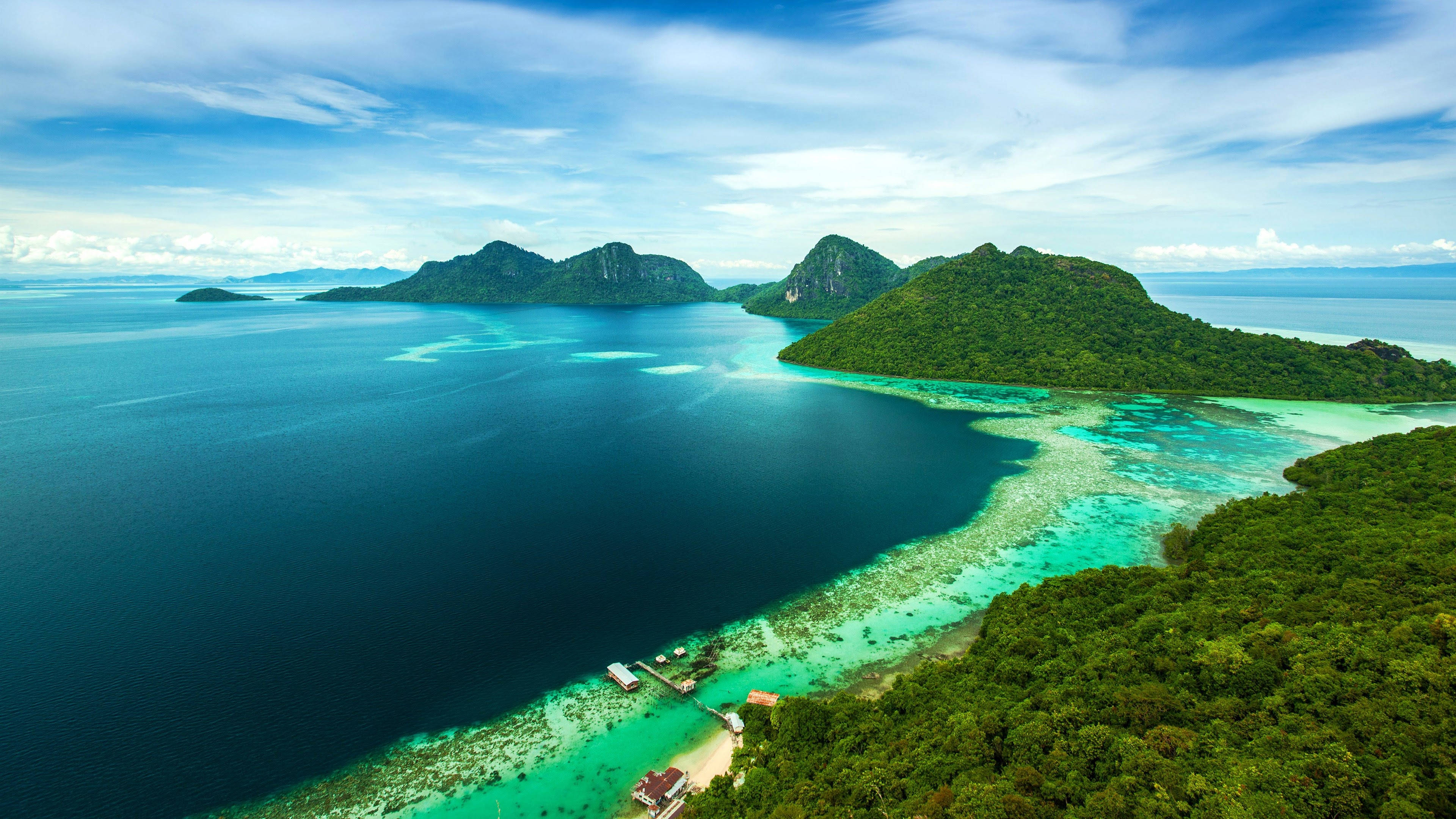 Island 桌布 壁紙 — 從空中俯瞰鬱鬱蔥蔥的綠色島嶼，周圍環繞著充滿活力的碧綠海水和深藍色海洋，天空部分多雲。