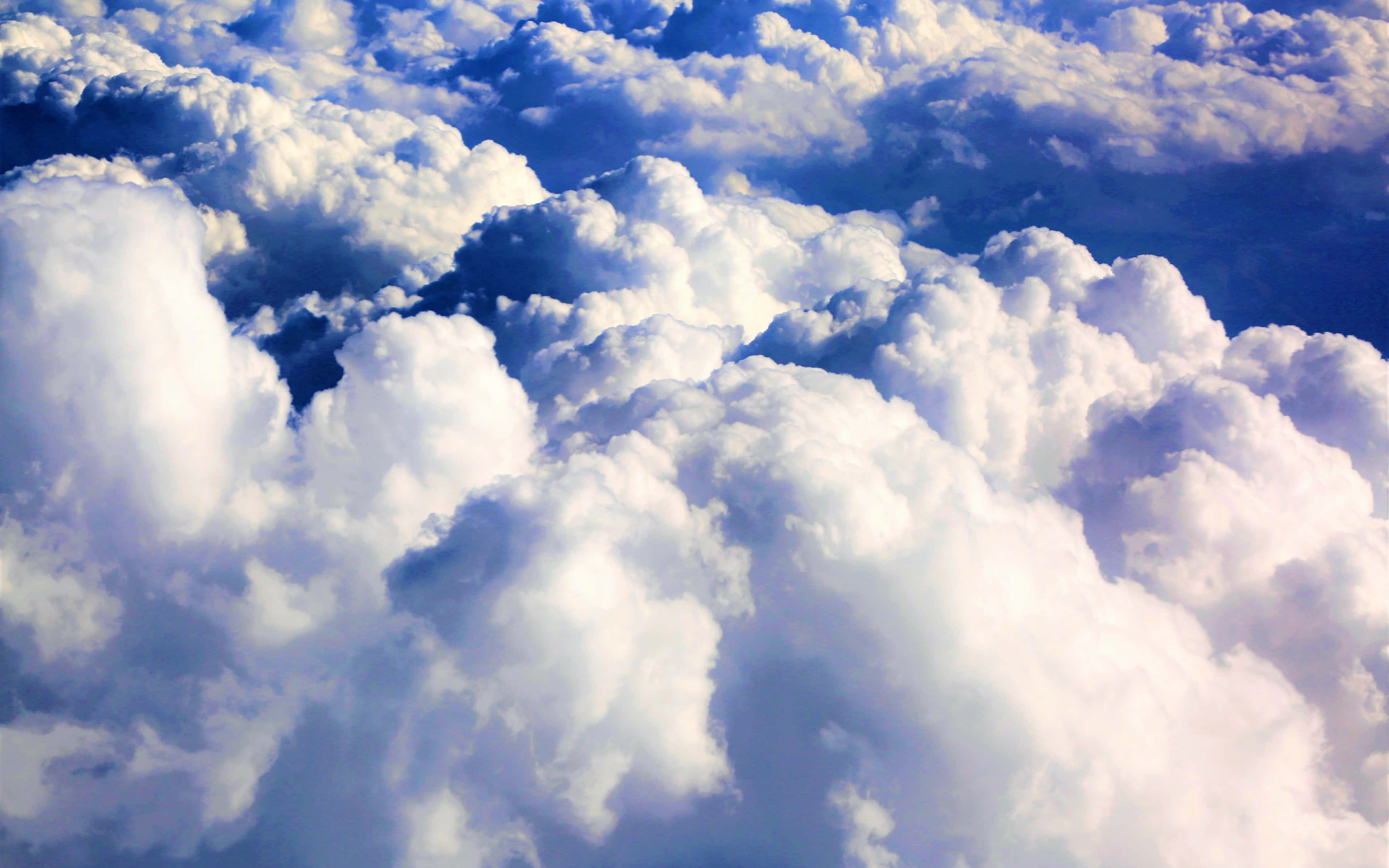 Clouds 4K 桌布 壁紙 — 從空中視角，大片蓬鬆的白雲在深藍色的天空中飄移。