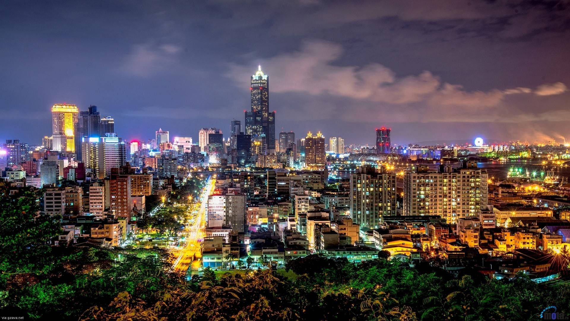 城市 桌布 壁紙 — 從綠色山頂觀賞充滿活力的夜景，閃爍的摩天大樓和燈火通明的街道。