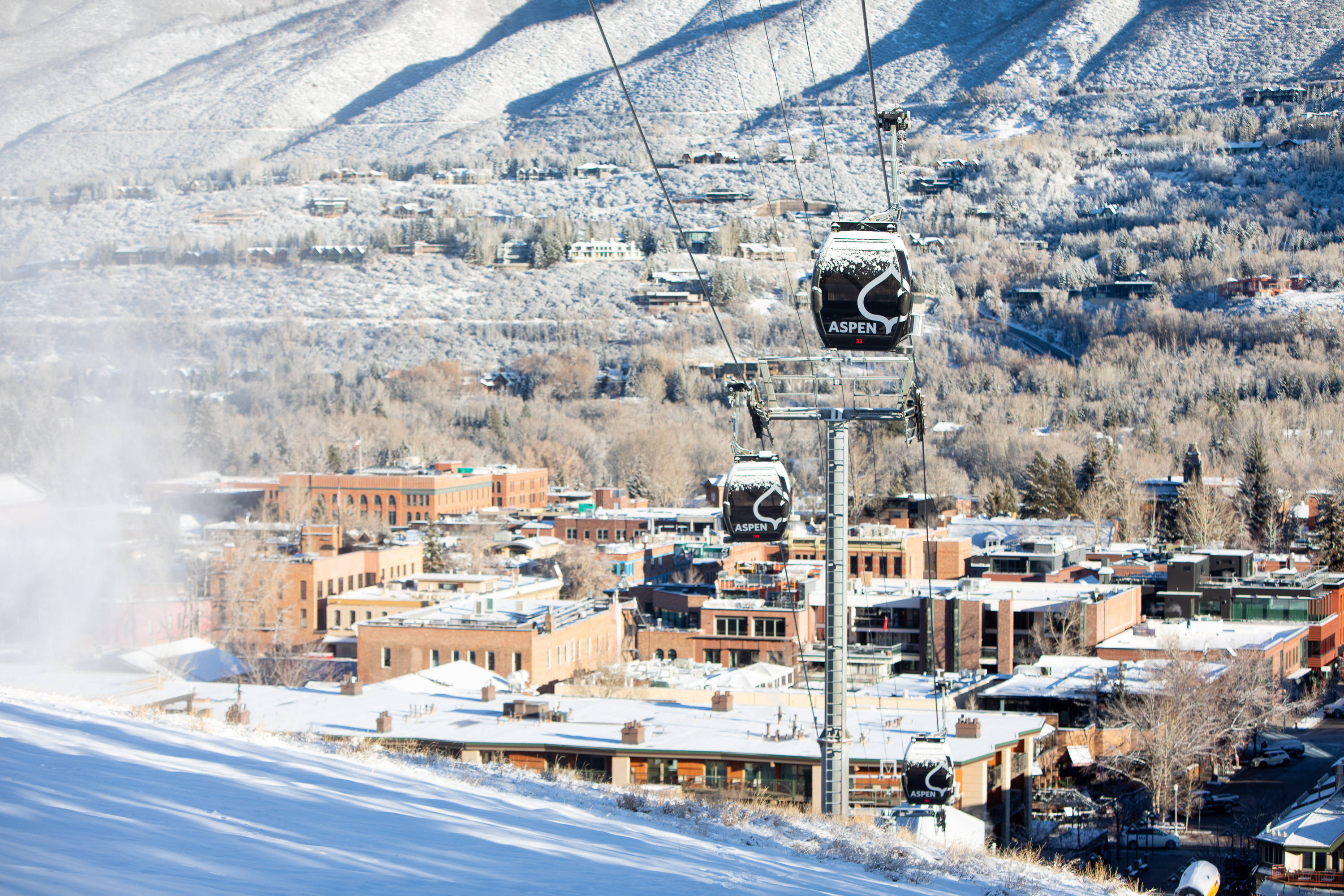 Colorado 桌布 壁紙 — 從纜車上看到的白雪覆蓋的阿斯彭滑雪度假小鎮，陽光照耀的山脈和積雪的屋頂。