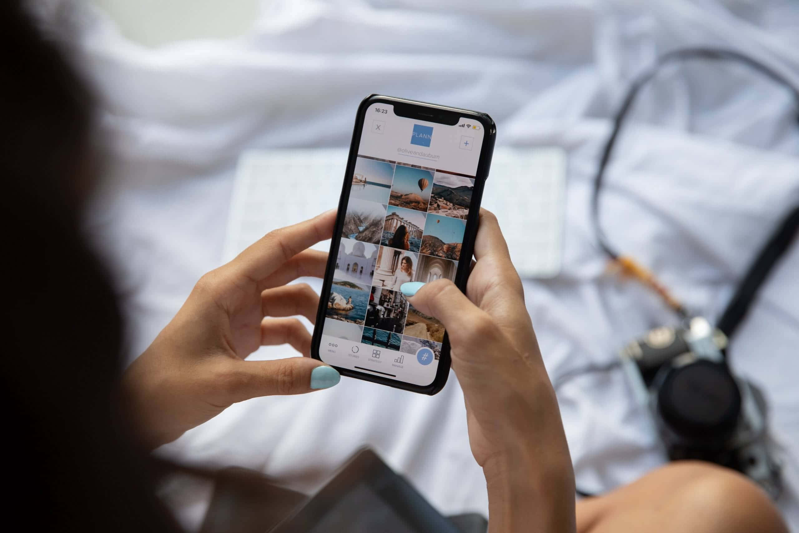 Instagram 桌布 壁紙 — 從肩膀上方看到一個人在床上放鬆時在智慧型手機上滾動瀏覽照片庫，附近有相機。