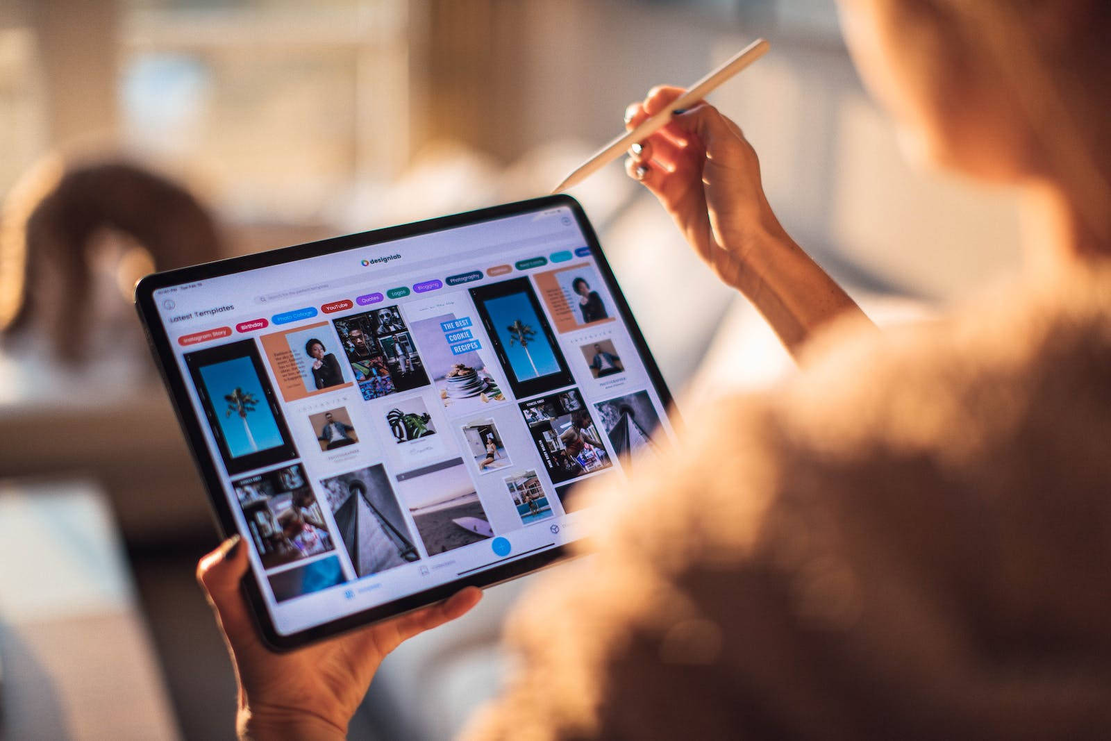Apple iPad Pro 桌布 壁紙 — 從肩膀上方視角，看到一個人在光線溫暖的室內空間中使用平板電腦瀏覽設計模板。