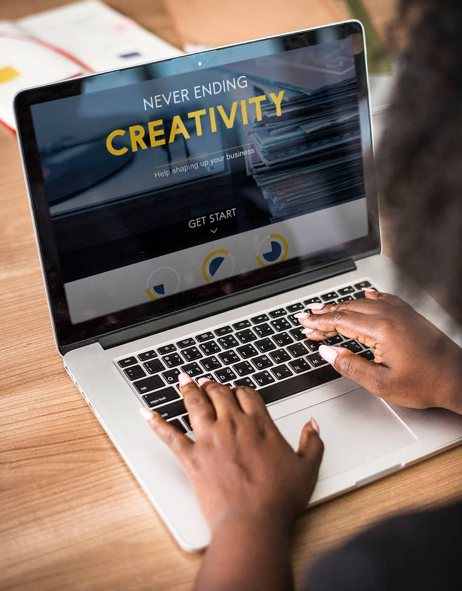 Best Laptop 桌布 壁紙 — 從肩膀後方觀看一個人在筆記型電腦上打字，顯示 'Never Ending Creativity' 商業網站。