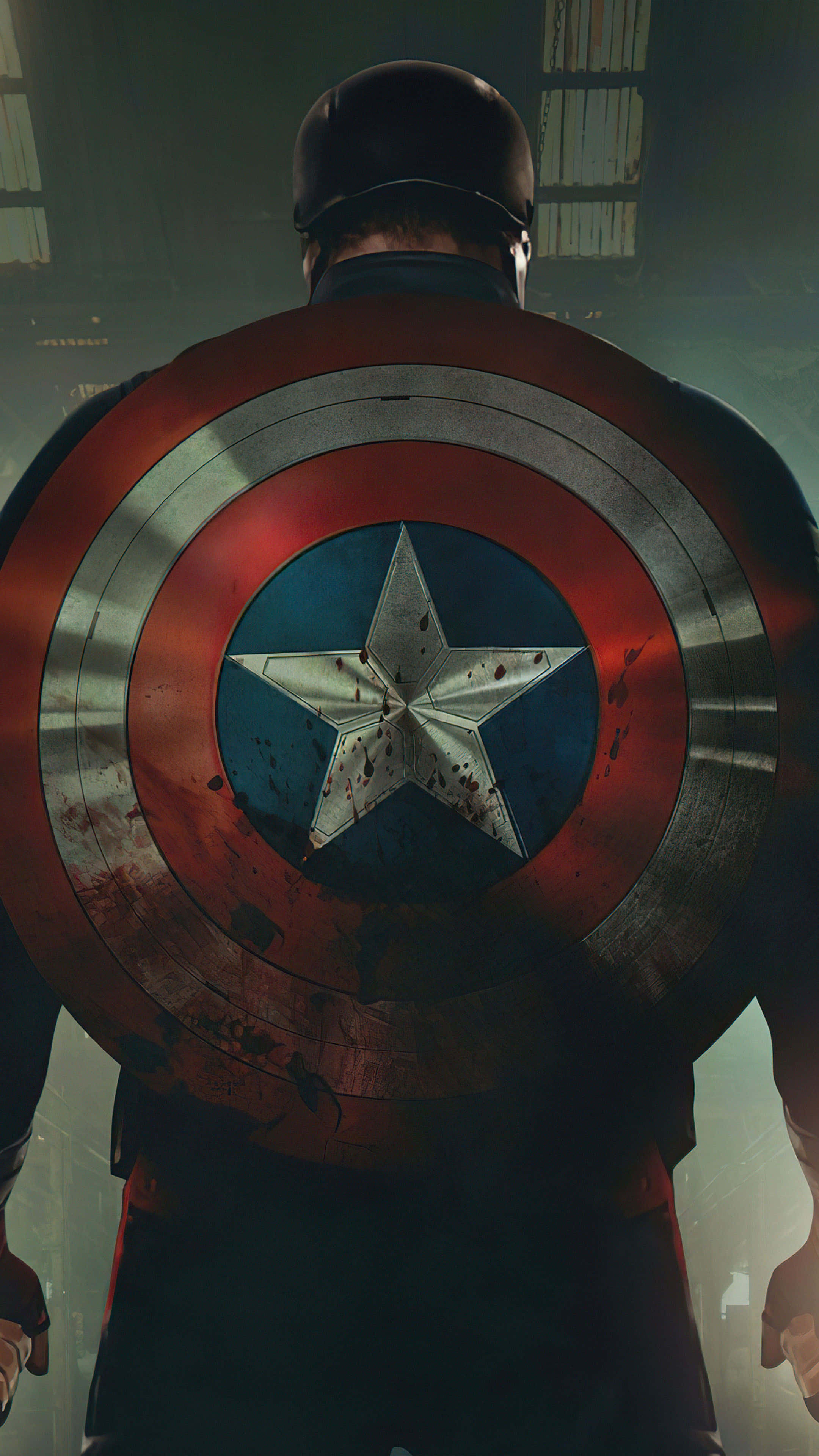 4K Captain America 桌布 壁紙 — 從背後看到美國隊長手持其標誌性的星條盾牌，盾牌上滿是戰鬥痕跡，身處昏暗的城市環境中。