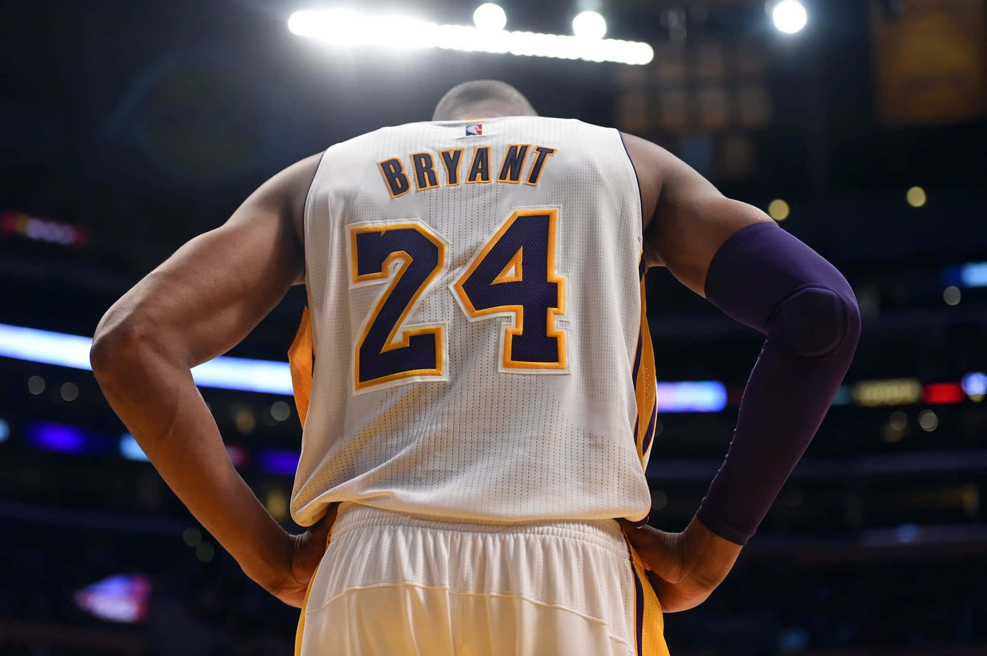 NBA 桌布 壁紙 — 從背後看到身穿白色24號球衣的籃球運動員柯比·布萊恩在場館燈光下手叉腰站立。