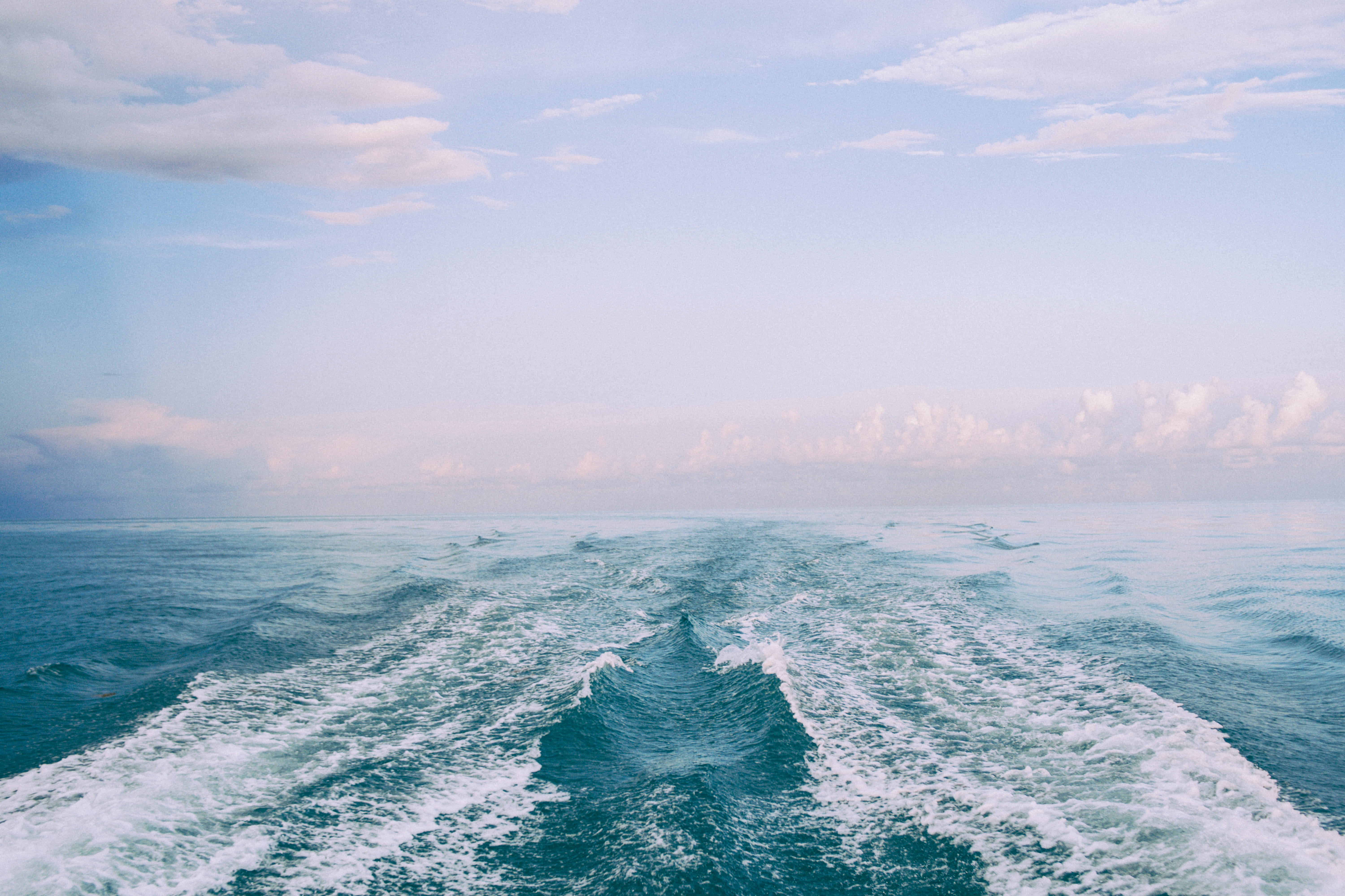 waves 桌布 壁紙 — 從船尾流觀看的寧靜海景，展現出在朦朧天空下的碧綠波浪和柔和粉彩雲朵。