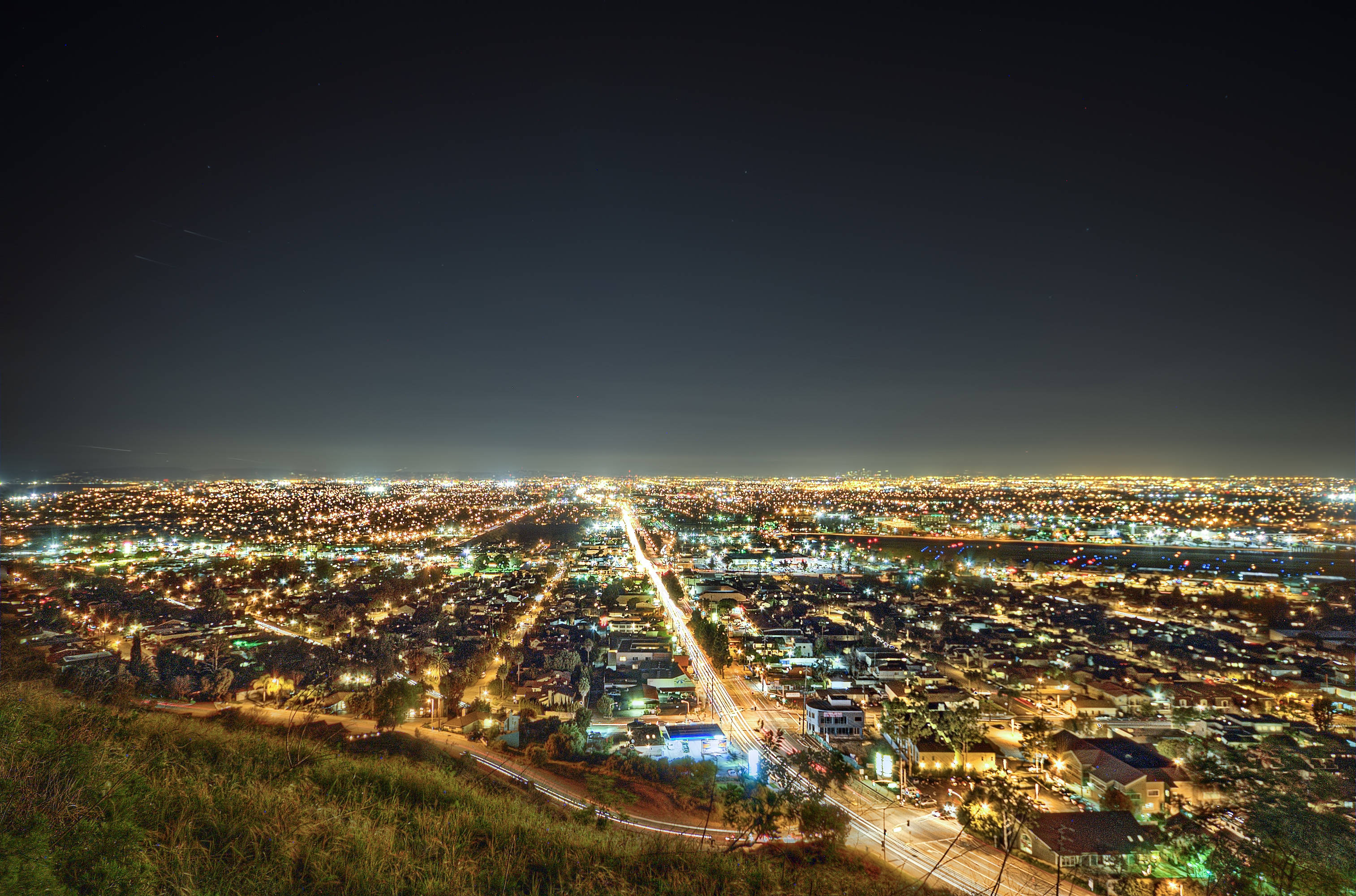 加州 桌布 壁紙 — 從草坡上觀賞的廣闊夜景城市景觀，發光的街燈和交通軌跡照亮了城市範圍。