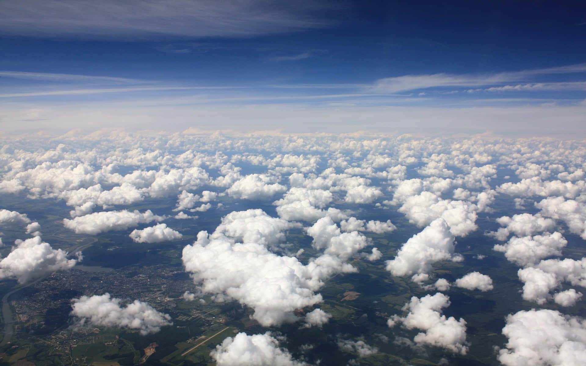 Clouds Aesthetics 桌布 壁紙 — 從蓬鬆白雲上方俯瞰的航拍視角，展現晴朗藍天下翠綠的風景和遠處的城鎮。
