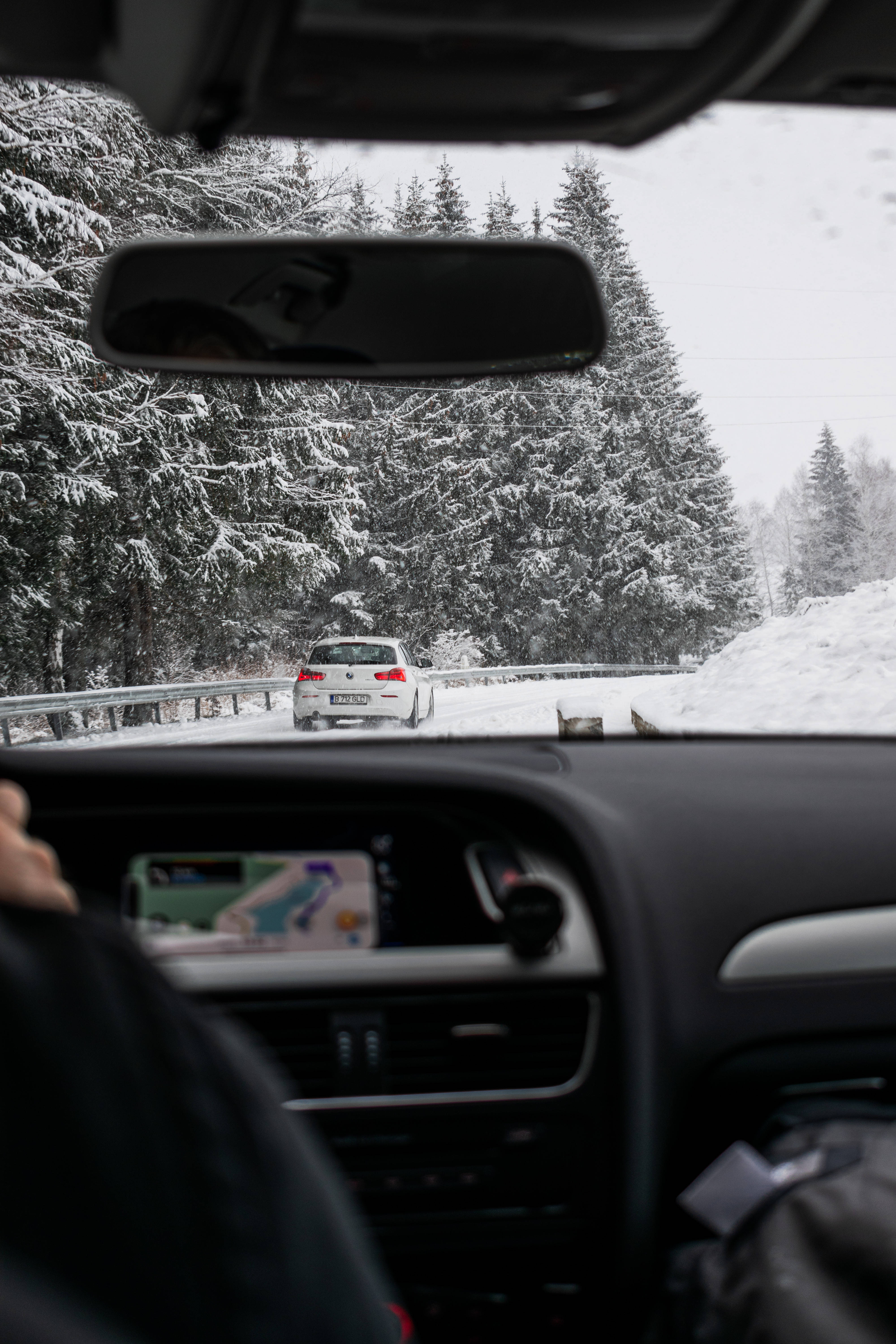 Amazing 桌布 壁紙 — 從車內看到的雪地森林道路，前方有一輛白色汽車，道路兩旁是積雪的松樹。