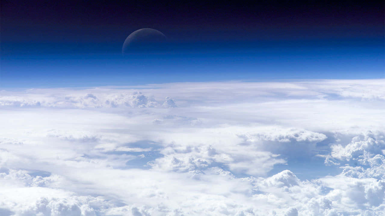 太空 桌布 壁紙 — 從雲層上方俯瞰的壯麗景色，一彎新月在深藍色的天空中閃耀。