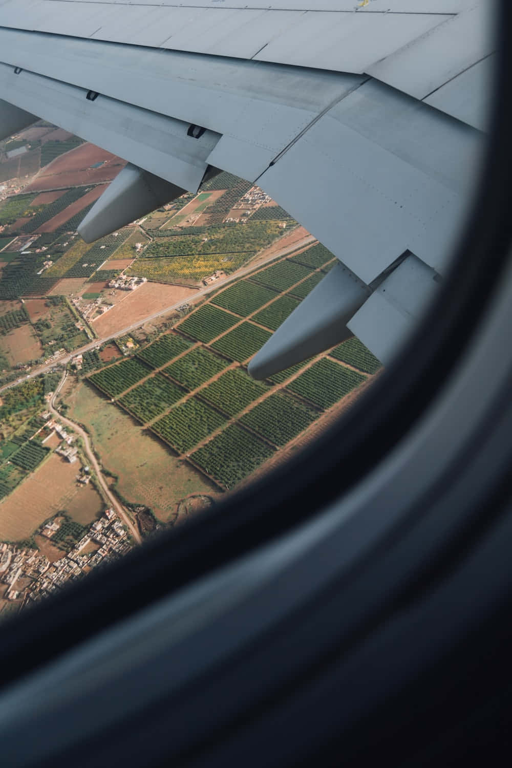 Airplane Window 桌布 壁紙 — 從飛機窗戶俯瞰，機翼下方是拼布般的農田和蜿蜒的道路。