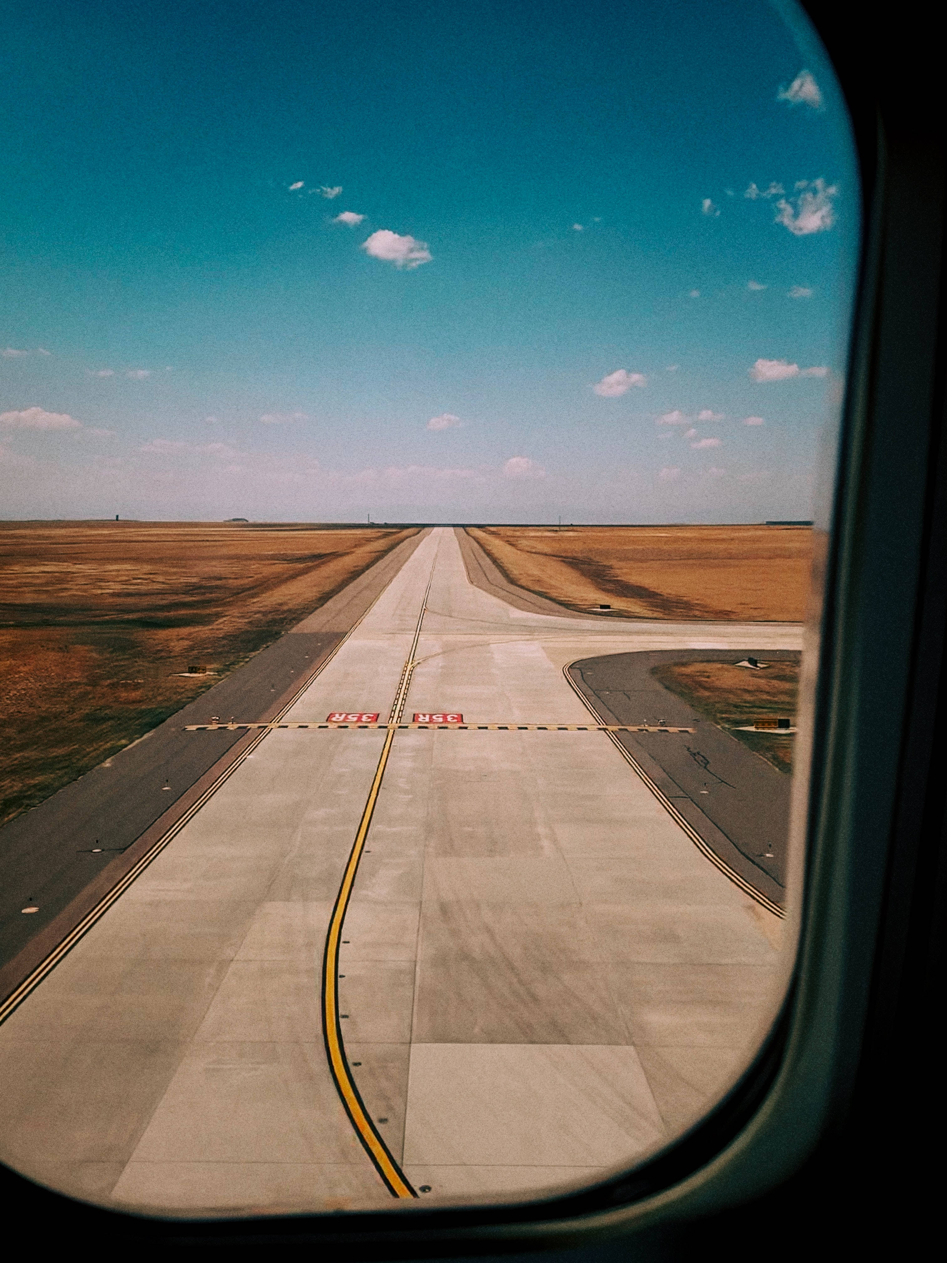 Runway 桌布 壁紙 — 從飛機窗戶俯瞰，跑道延伸至平坦的金色平原，藍天白雲清晰可見。