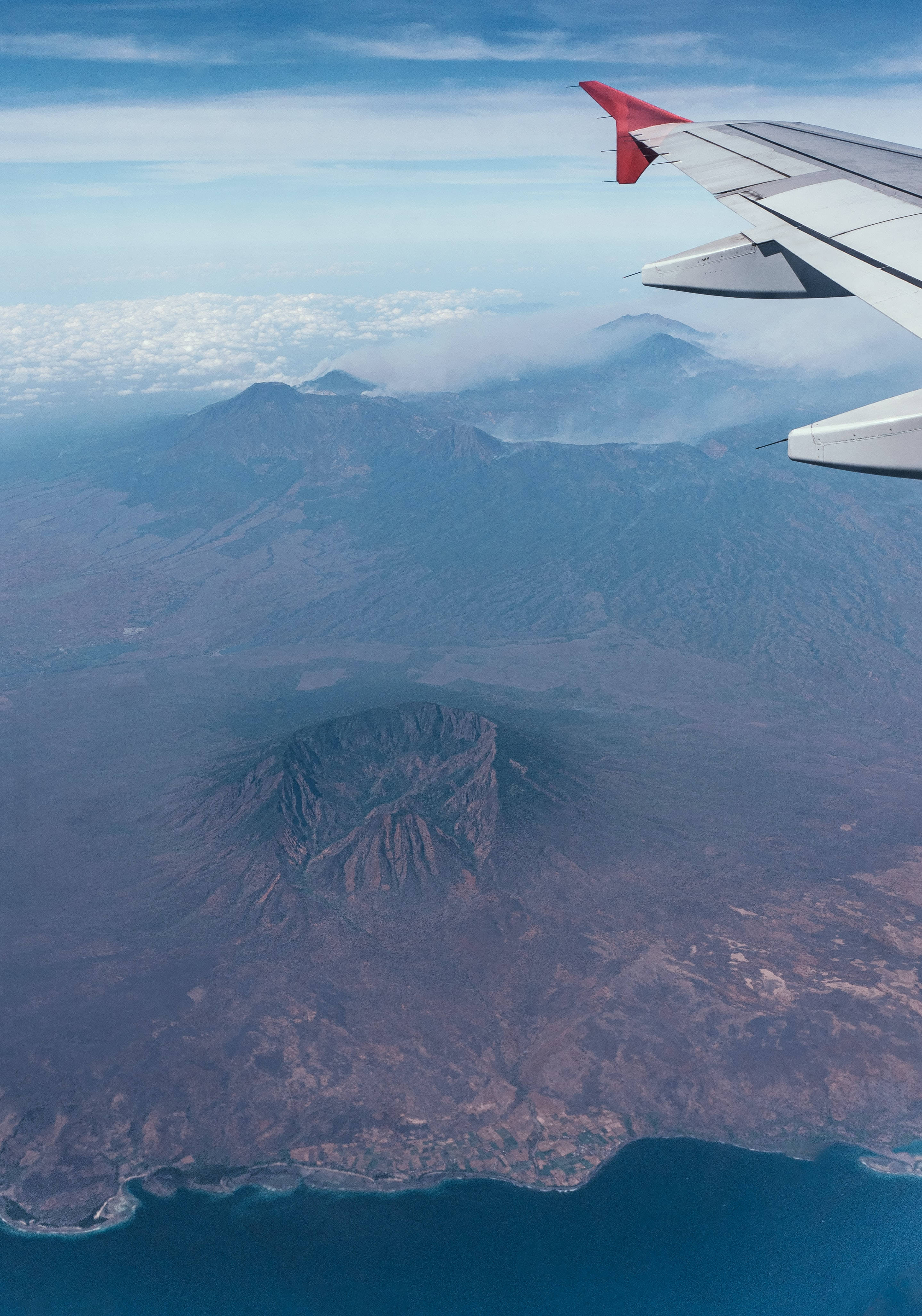 飛機 桌布 壁紙 — 從飛機窗戶俯瞰崎嶇的火山島，下方有深火山口和海岸懸崖。