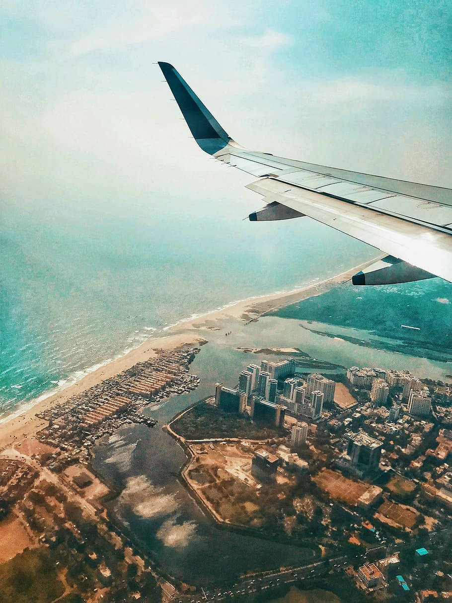 Chennai 桌布 壁紙 — 從飛機窗戶俯瞰的空中景觀，顯示機翼下方沿海城市、藍綠色海洋和沙灘。