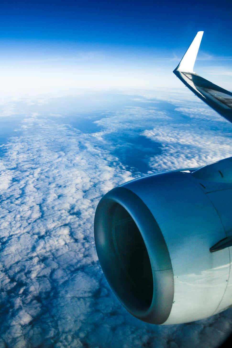 Airplane Window 桌布 壁紙 — 從飛機窗戶俯瞰的空中視角，顯示噴射引擎和機翼在清澈天空下無盡的藍色雲層之上。