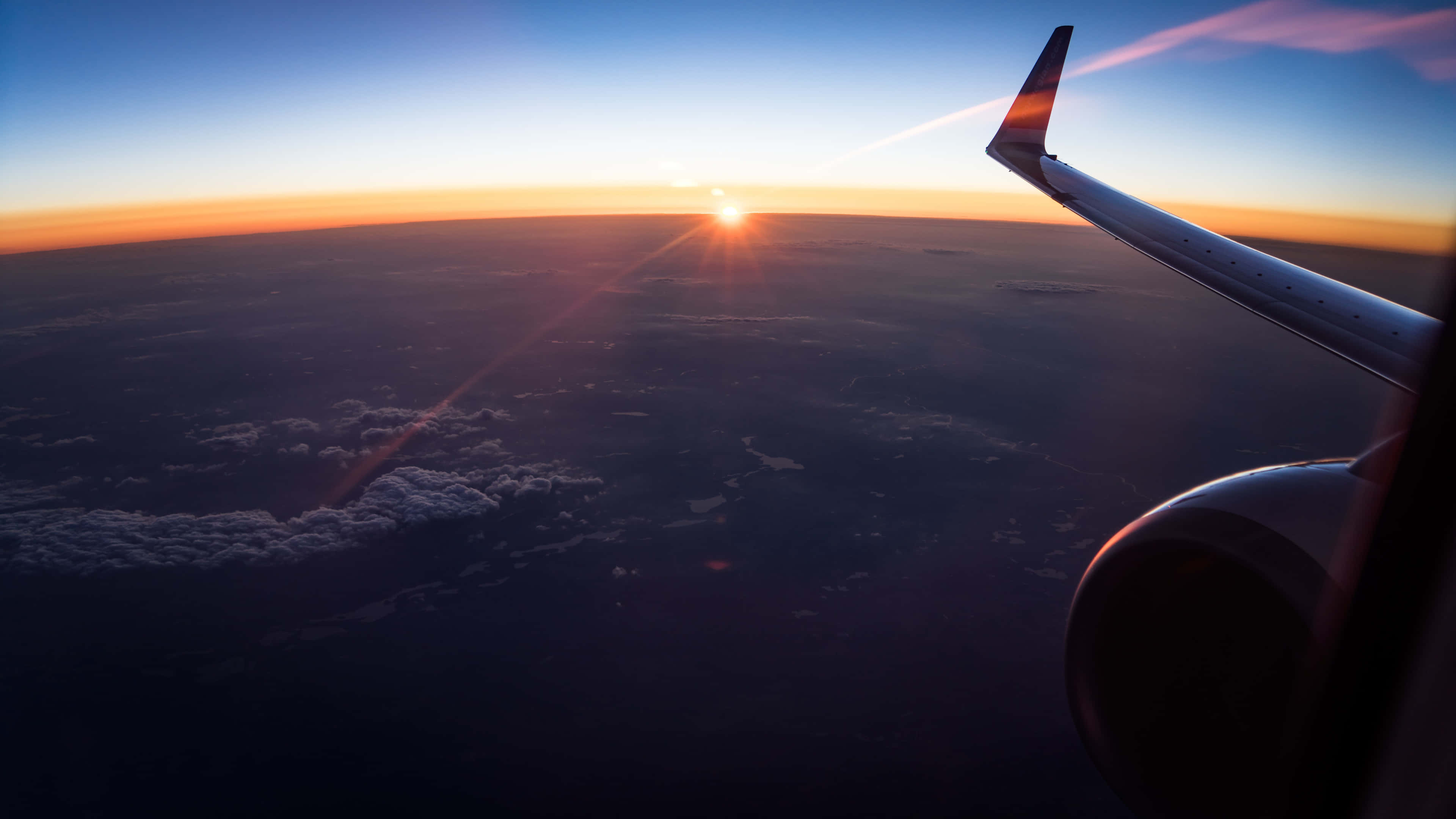 雲朵 桌布 壁紙 — 從飛機窗戶看到夕陽在雲層上發光，機翼和引擎清晰可見。