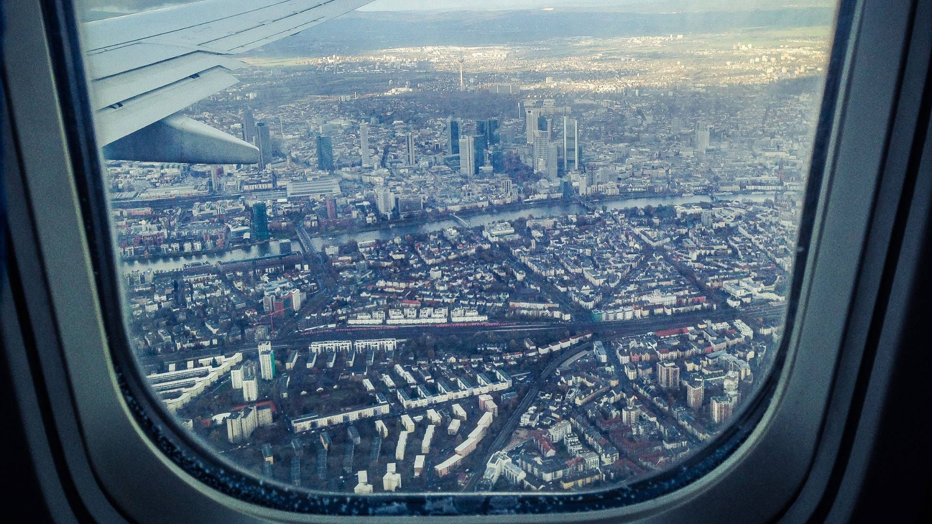 城市風景 桌布 壁紙 — 從飛機窗戶看到廣闊城市景觀的鳥瞰圖，機翼可見。