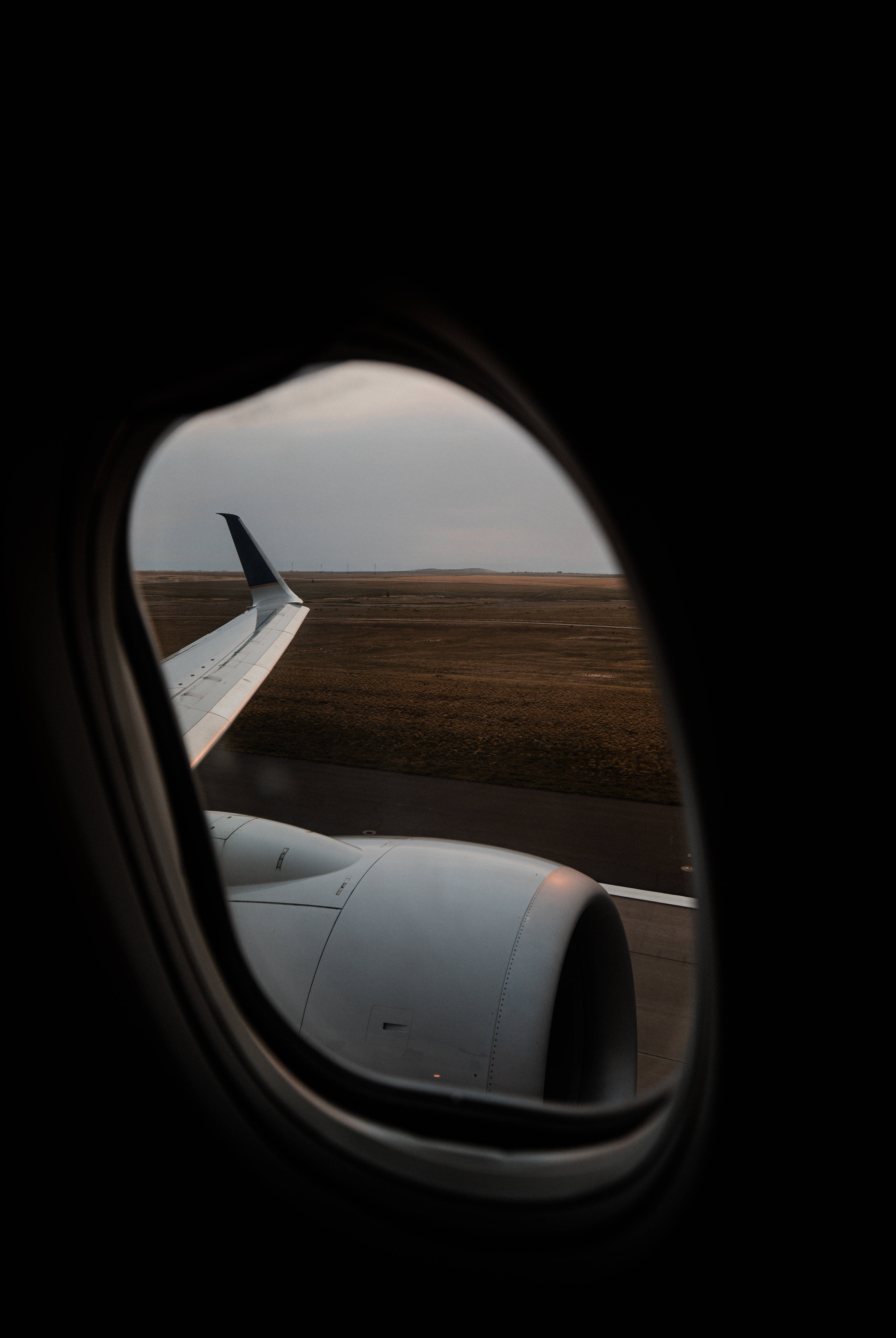 Plane 桌布 壁紙 — 從飛機窗戶看到的景色，顯示機翼、引擎和跑道，天空多雲，黃昏時分。