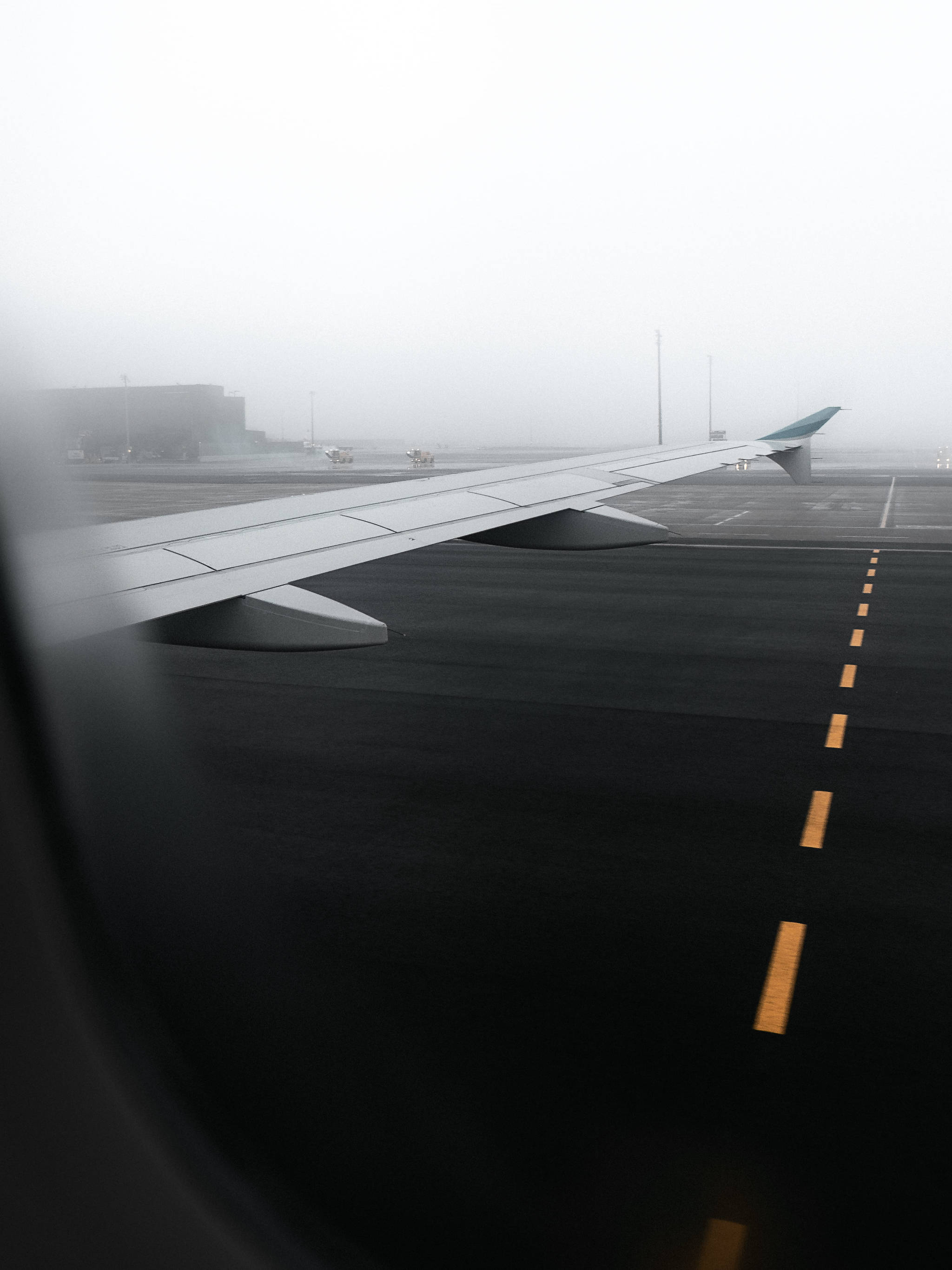 Runway 桌布 壁紙 — 從飛機窗戶看到的霧氣瀰漫的機場停機坪，機翼延伸在黃色跑道標記上方。