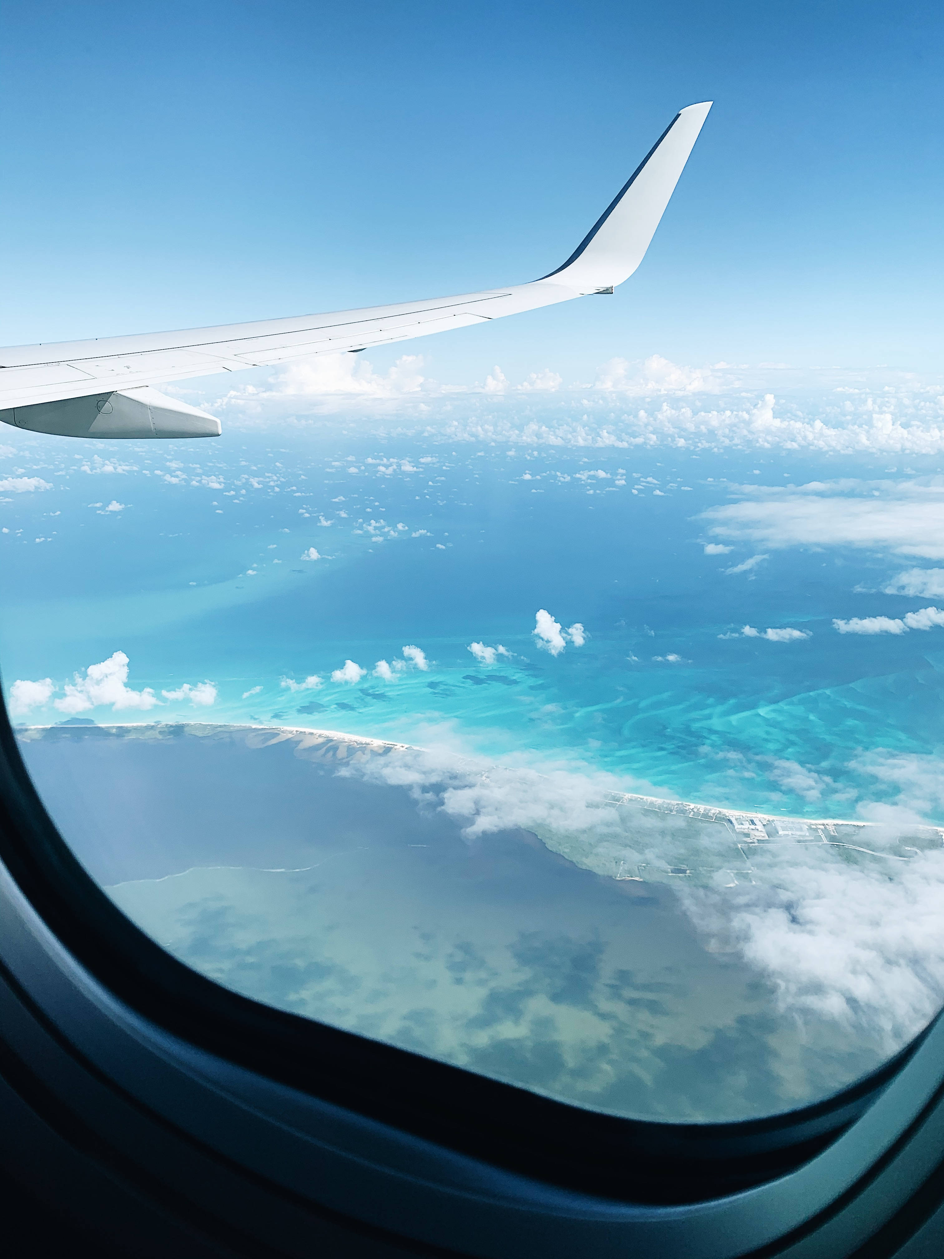 旅行 桌布 壁紙 — 從飛機窗戶看到的飛機機翼，俯瞰下方的碧綠海洋和白色雲層。