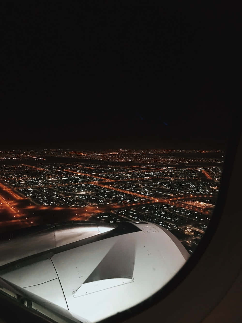 Airplane Window 桌布 壁紙 — 從飛機窗戶看到的飛機機翼，俯瞰著一座被溫暖夜燈照亮、不斷擴展的城市。