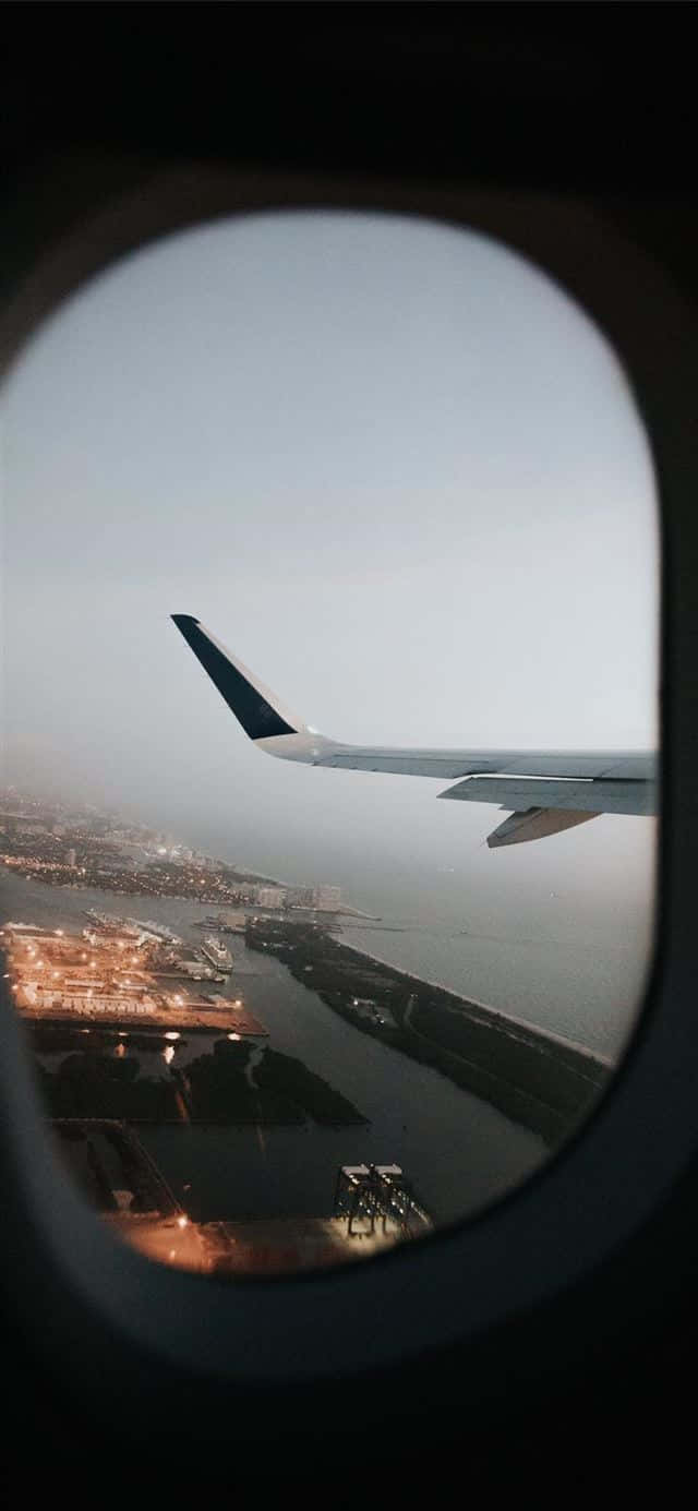 Plane 桌布 壁紙 — 從飛機窗戶看到的飛機機翼，俯瞰黃昏時分的沿海城市和港口。
