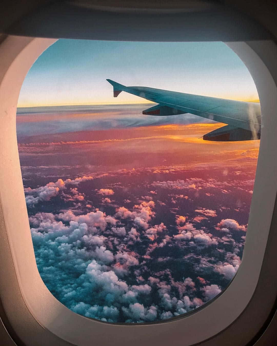 Airplane Window 桌布 壁紙 — 從飛機窗戶看到的飛機翼剪影，映襯著充滿活力的日落，將雲彩染成橙色、粉紅色和藍綠色。