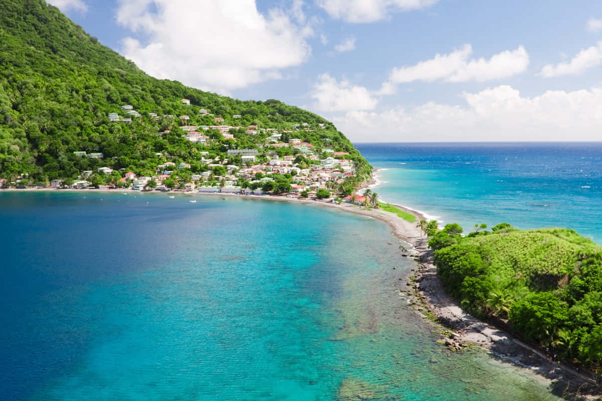Caribbean Island 桌布 壁紙 — 從高空俯瞰，一個充滿活力的綠松石海灣蜿蜒環繞著翠綠的山丘，山丘上點綴著色彩繽紛的房屋，上方是明亮的藍天。