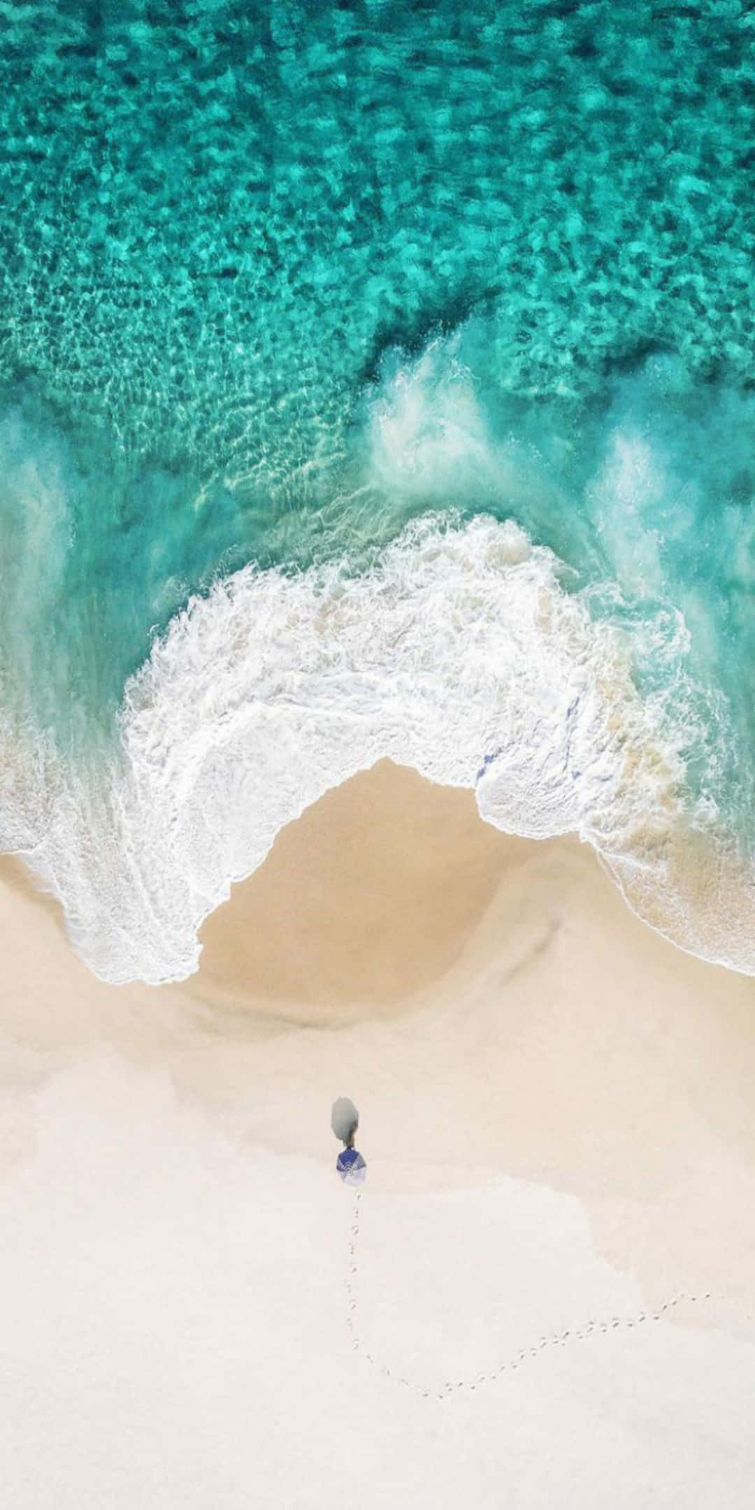 Pixel 3 Beach 桌布 壁紙 — 從高空俯瞰，一個孤獨的人走在純淨的白沙上，而藍綠色的海浪在他們周圍形成完美的弧線。