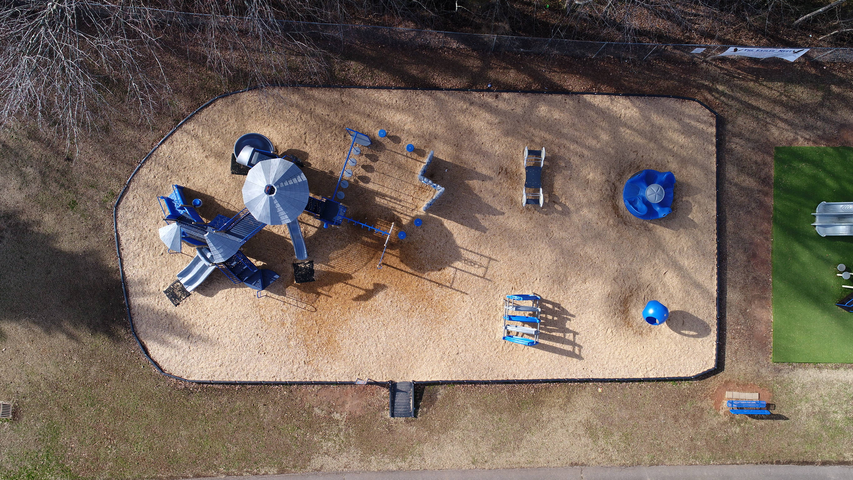 Playground 桌布 壁紙 — 從高空俯瞰，一個藍色遊樂場結構被木屑和光禿禿的樹木包圍，正值深秋。
